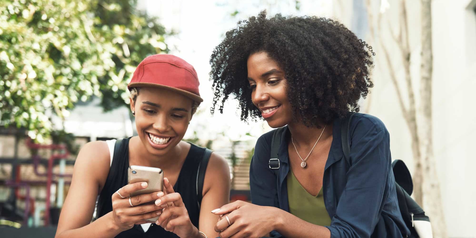 Titelbild für Infoseite “Hochschulwechsel”: Zwei Studentinnen sitzen draußen und schauen gemeinsam auf ein Smartphone