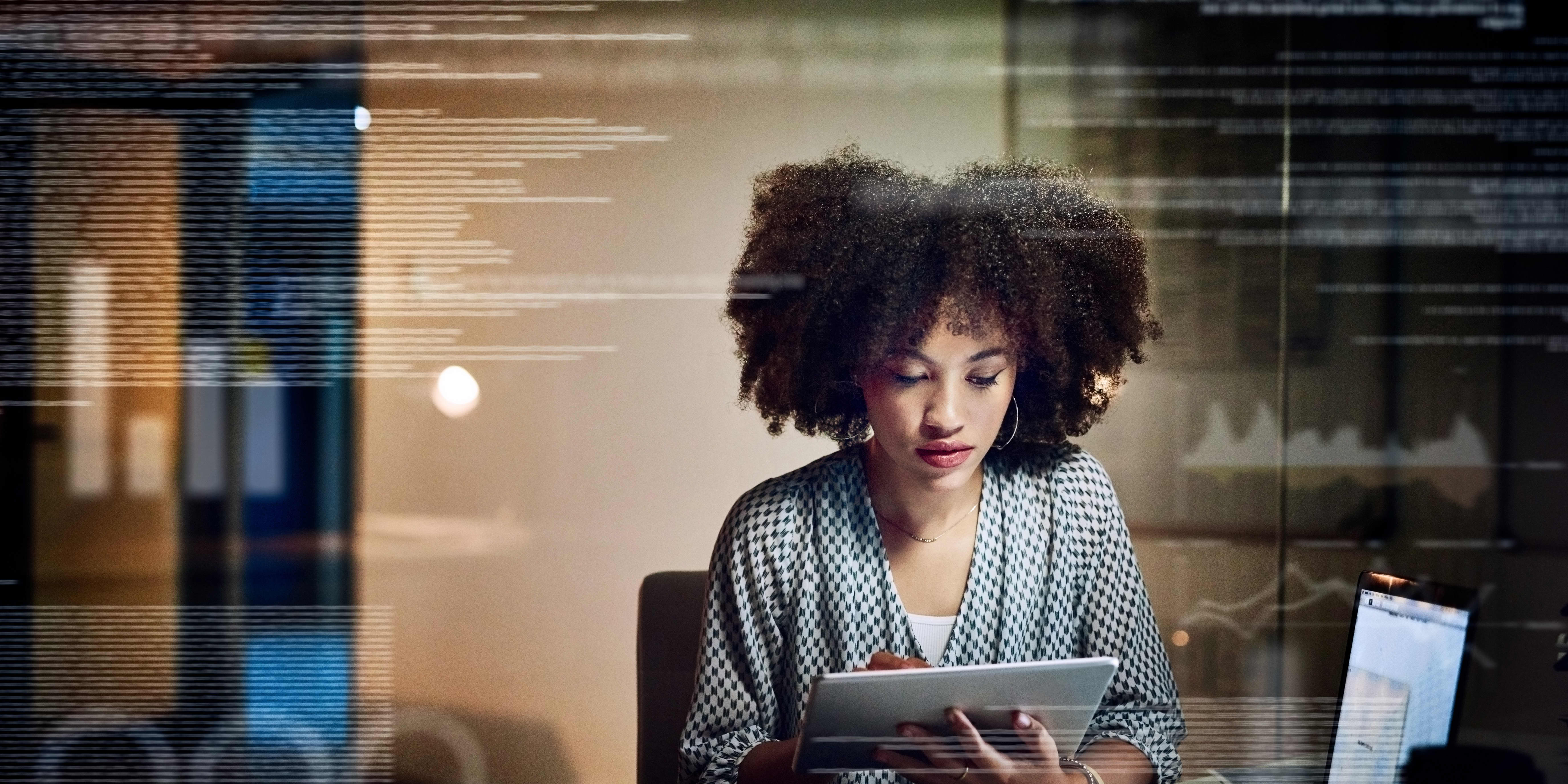 A young woman with curly hair works intently on a tablet in a modern office setting, symbolizing the first steps toward building a career in AI and technology.