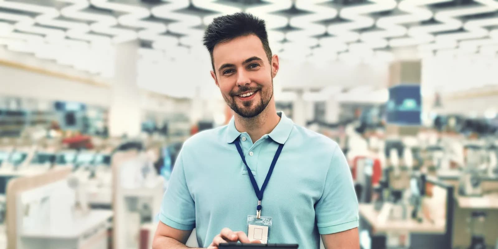 Titelbild für Infoseite “duales Studium BWL Handelsmanagement": Lächelnder dualer Student im Elektronikgeschäft mit Tablet in der Hand