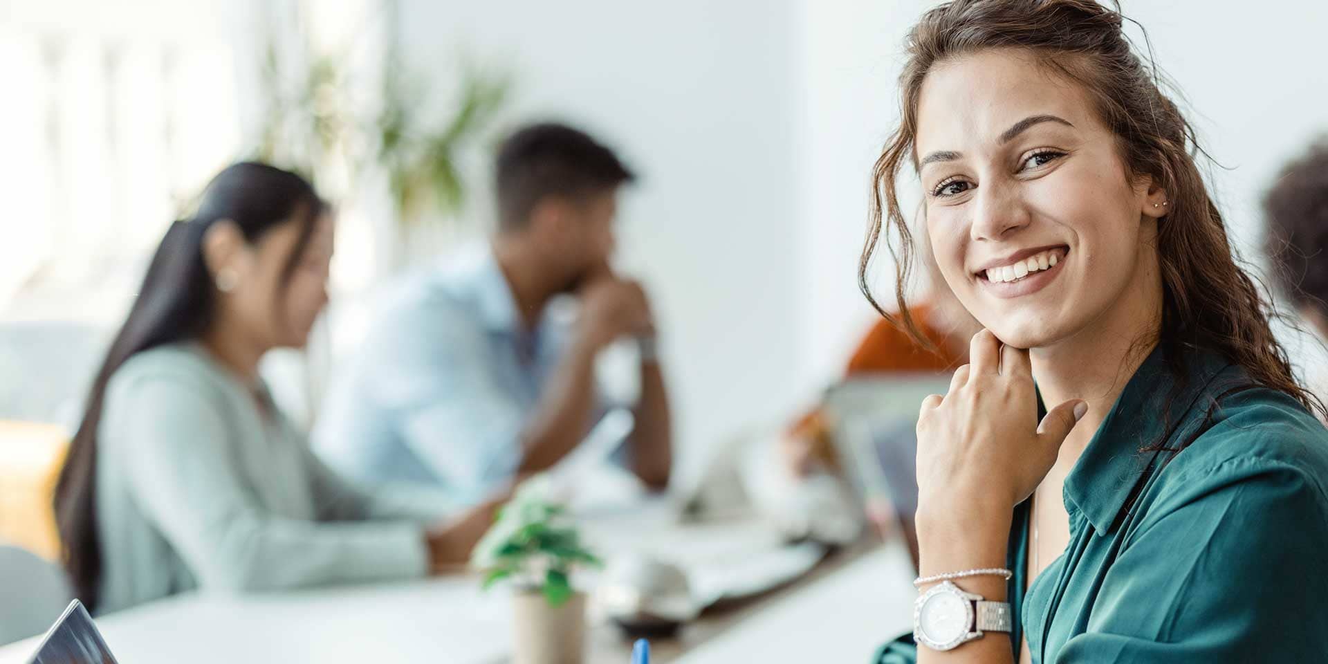 Titelbild zum Artikel "Erster Arbeitstag": Lächelnde Frau mit Laptop im Büro mit Kollegen