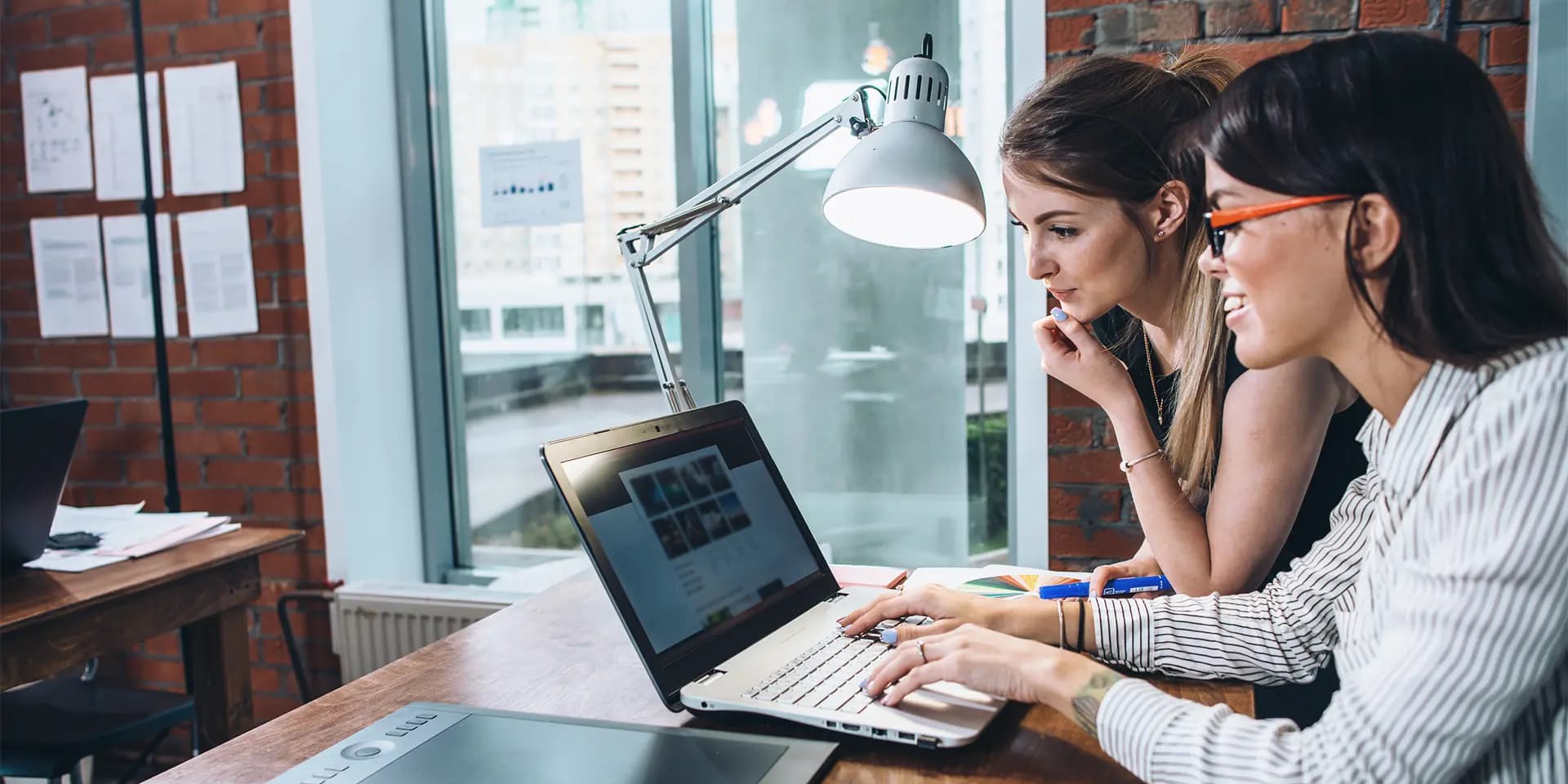 Titelbild zum Artikel "Wie baue ich ein Portfolio auf?": Zwei Frauen schauen in ein Laptop über das Portfolio