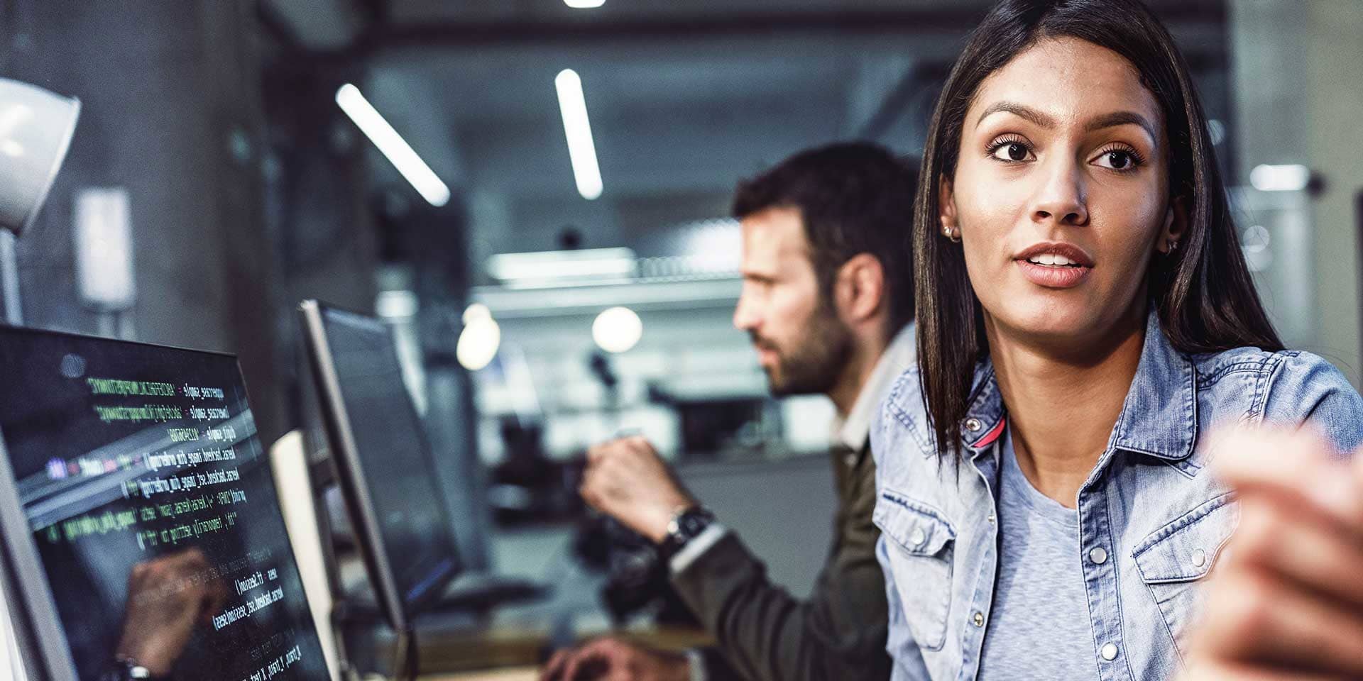 Programmiererin sitzt am PC im Büro mit anderen Kollegen