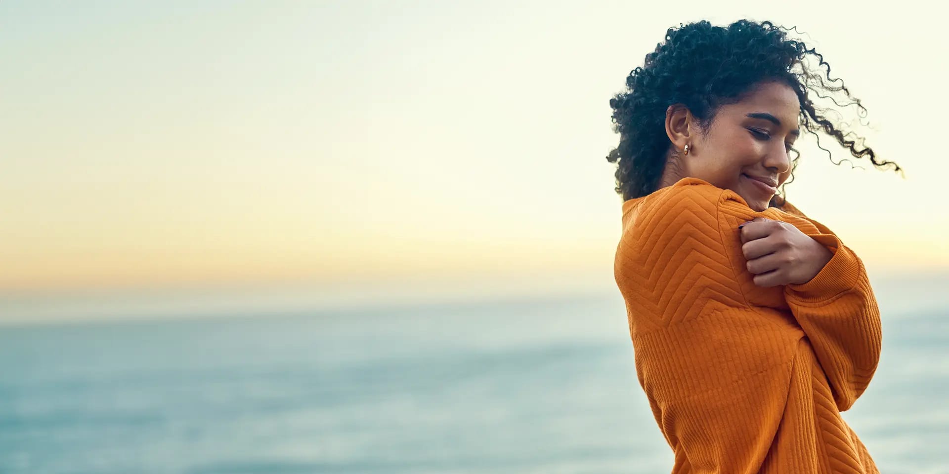 Titelbild zum Artikel "Selbstliebe & Affirmation": Selbstbewusste Frau umarmt sich selbst am Meer