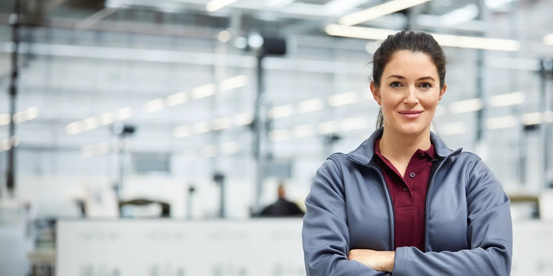 Titelbild für Artikel zum Techniker Studium: Selbstbewusste junge Frau steht in einer Produktionshalle