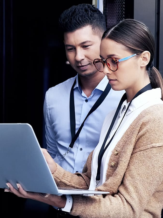 Two professionals review data on a laptop in a server room, representing the career and salary potential in computer science for 2024.