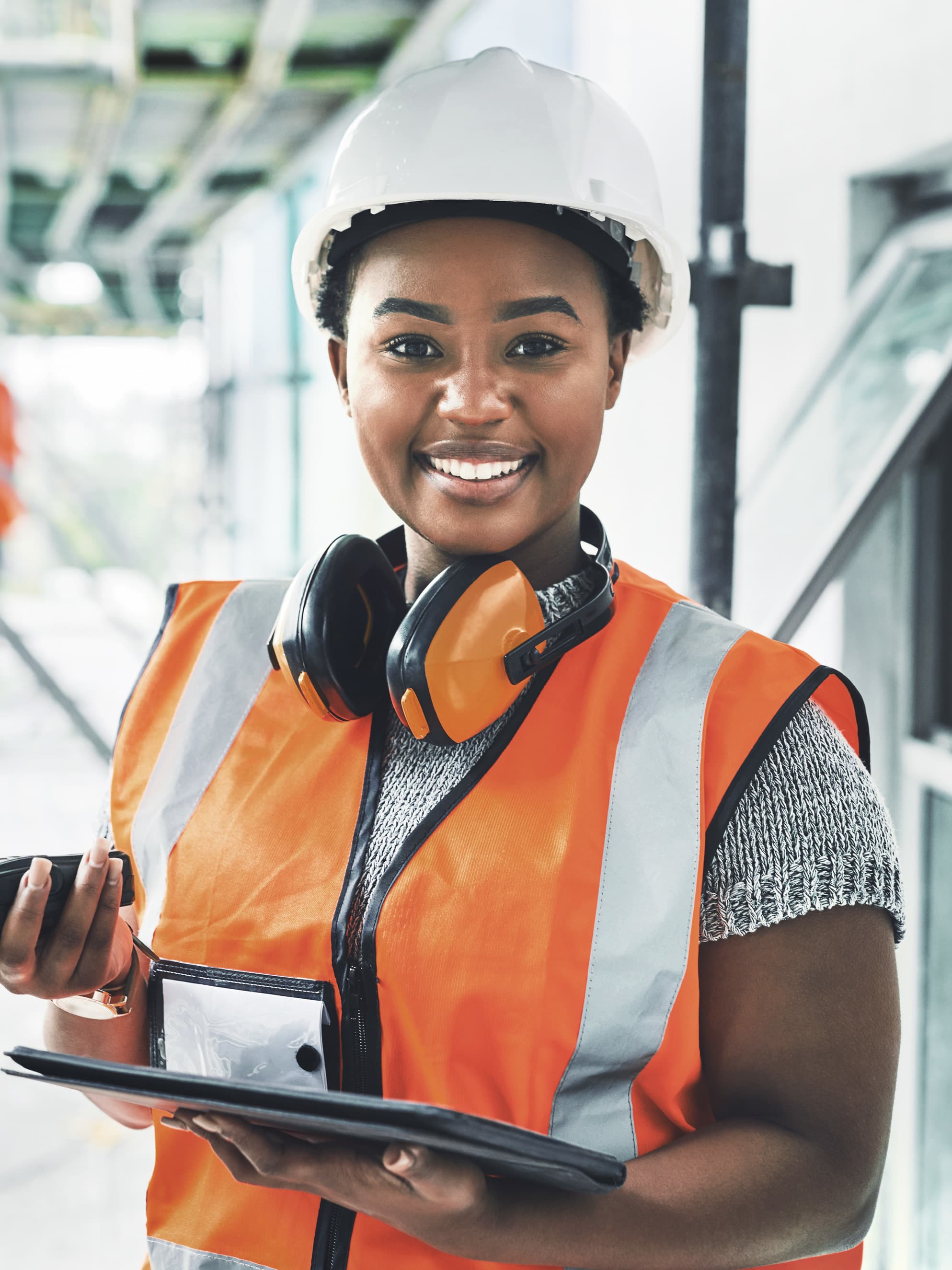 Titelbild für Infoseite “duales Studium Bauingenieurwesen”: Lachende duale Studentin mit Sicherheitsweste, Helm und Funkgerät auf einer Baustelle, AI-generated