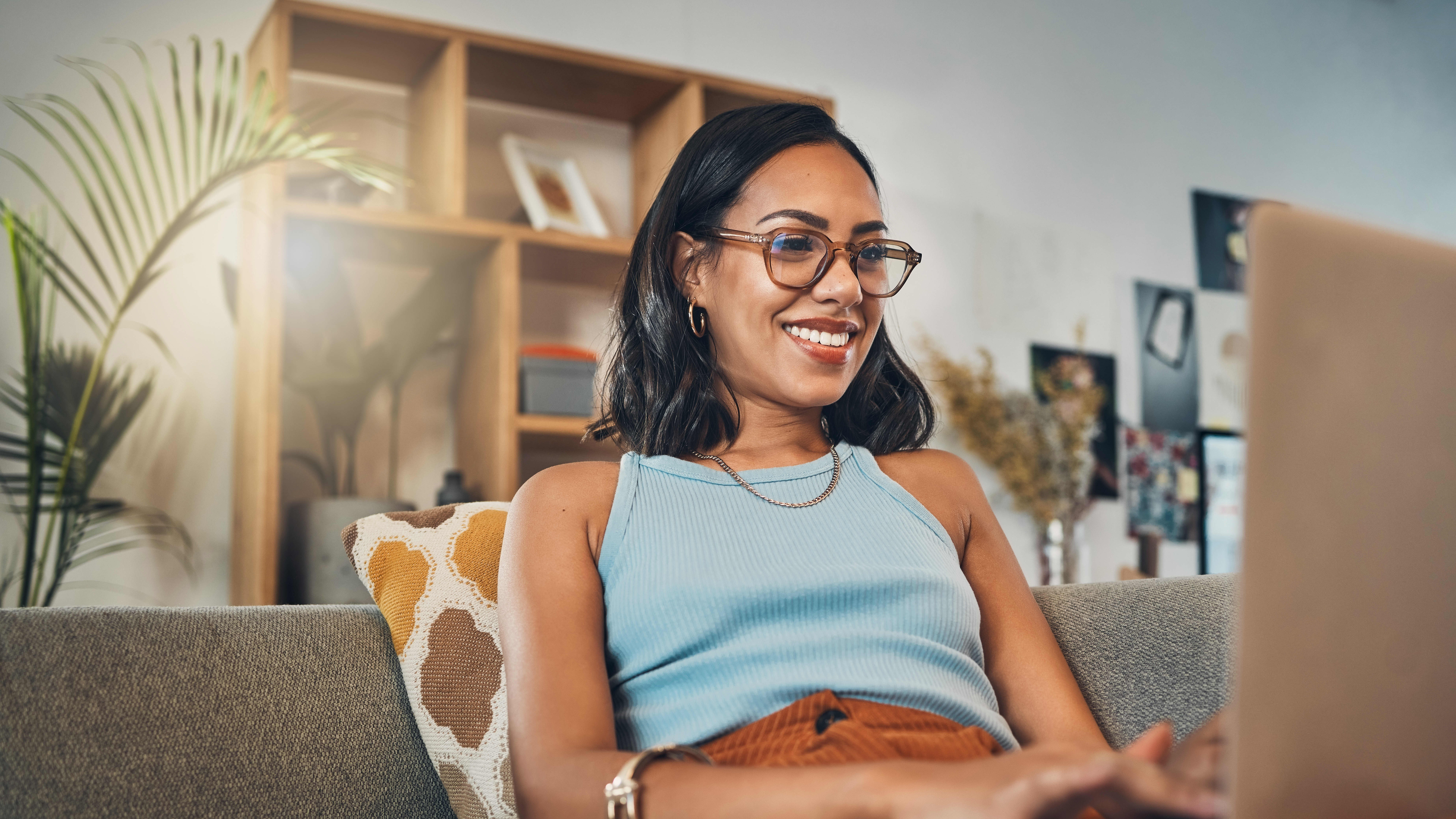 Woman with glasses and a casual blue shirt, looking at her laptop, presumable learning about the specific skills she could gain with micro-credentials.