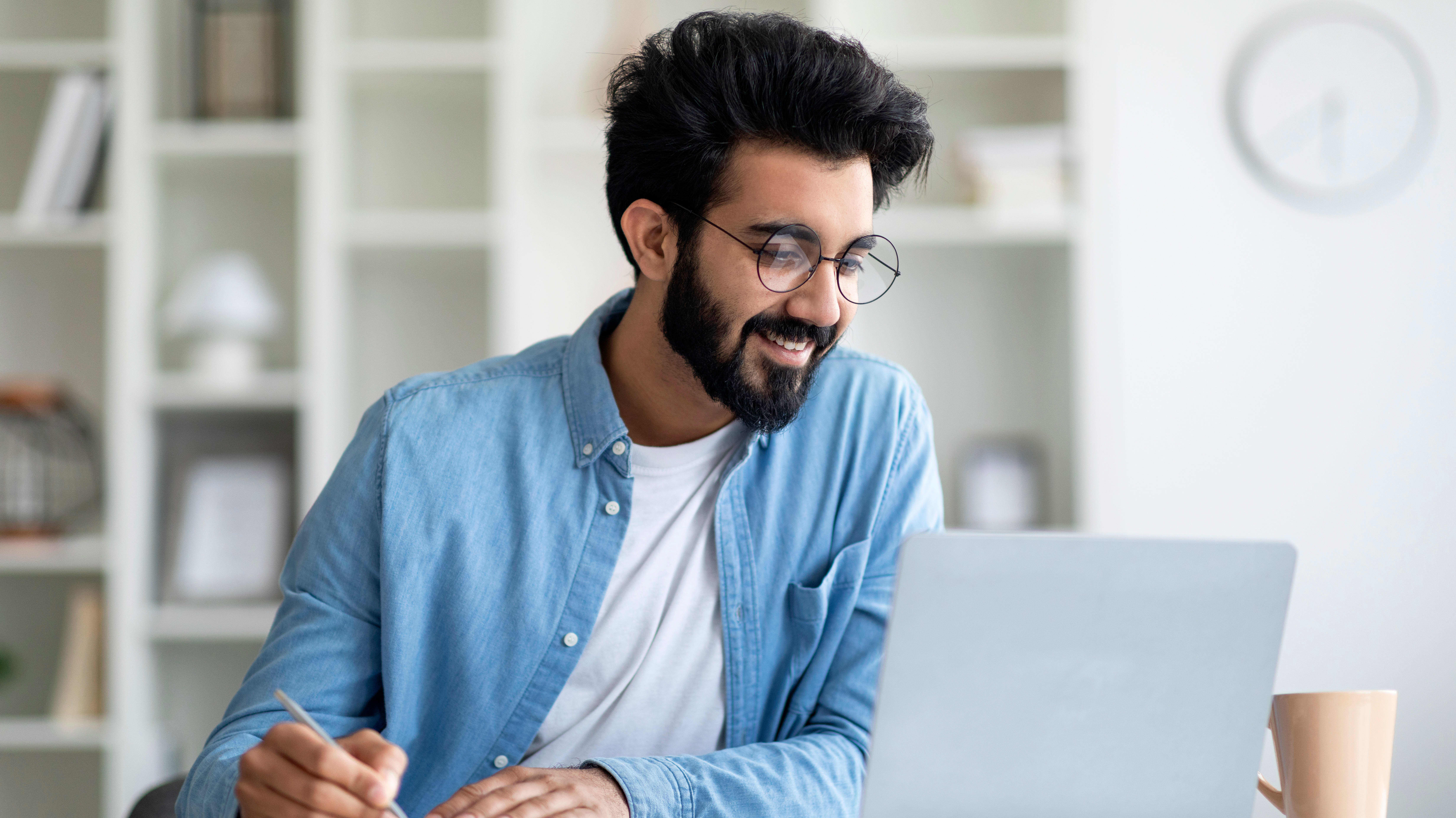 Man wearing glasses and a casual denim shirt, working on his mb degree online, while in his home office.
