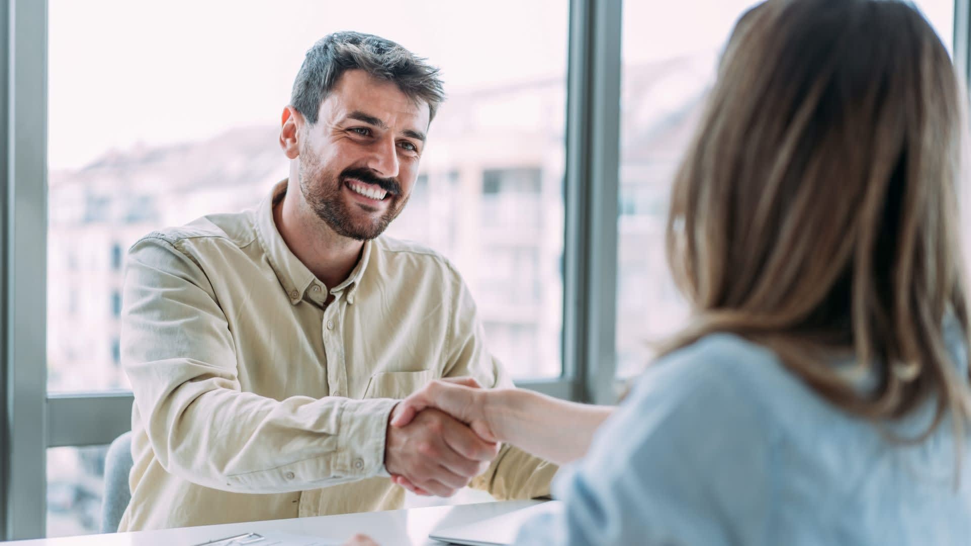 A man is sat in a meeting about entrepreneurial strategies, shaking hands with a woman sat opposite him