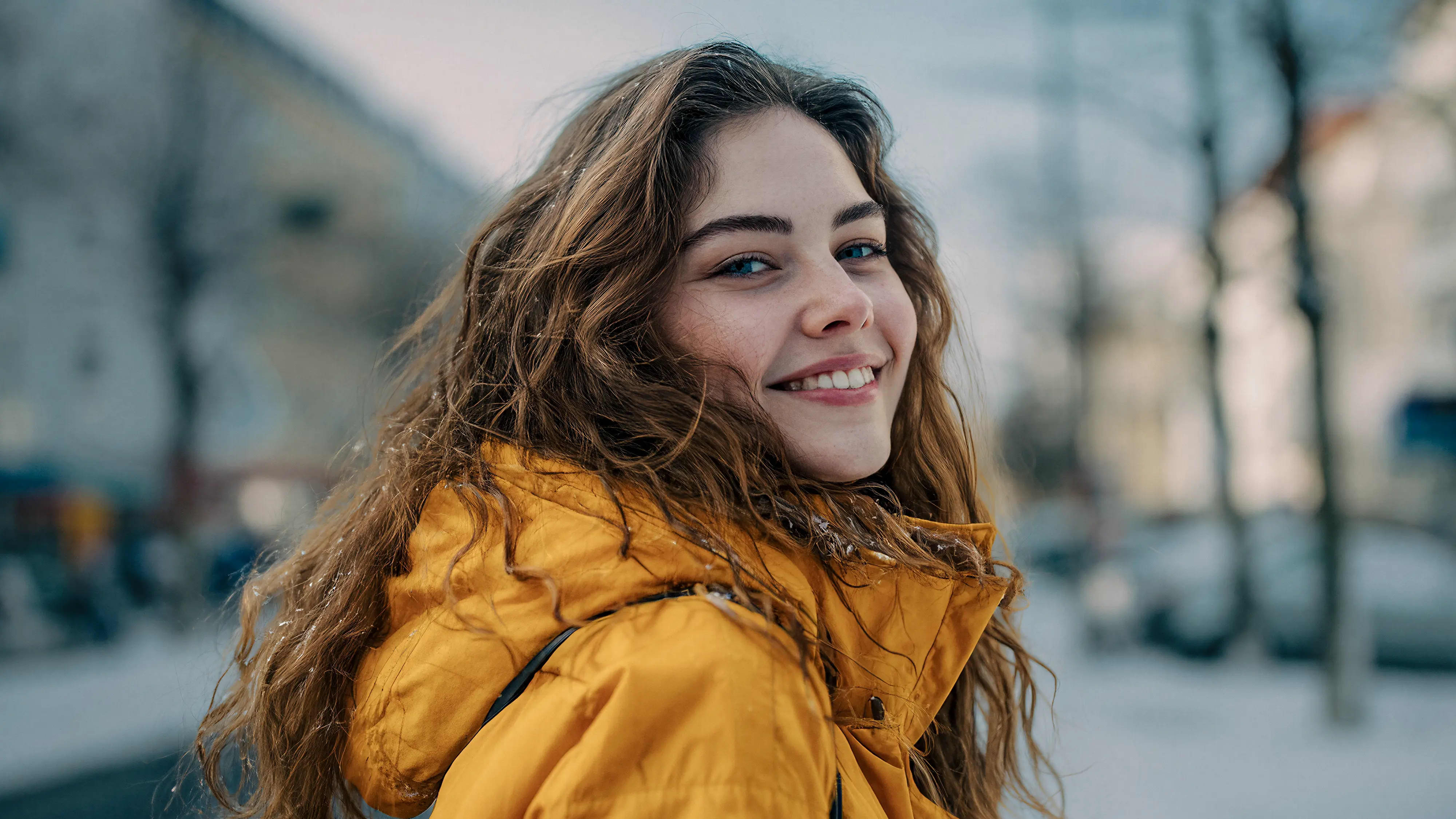Junge Frau mit gelbem Mantel lächelt in urbaner Umgebung