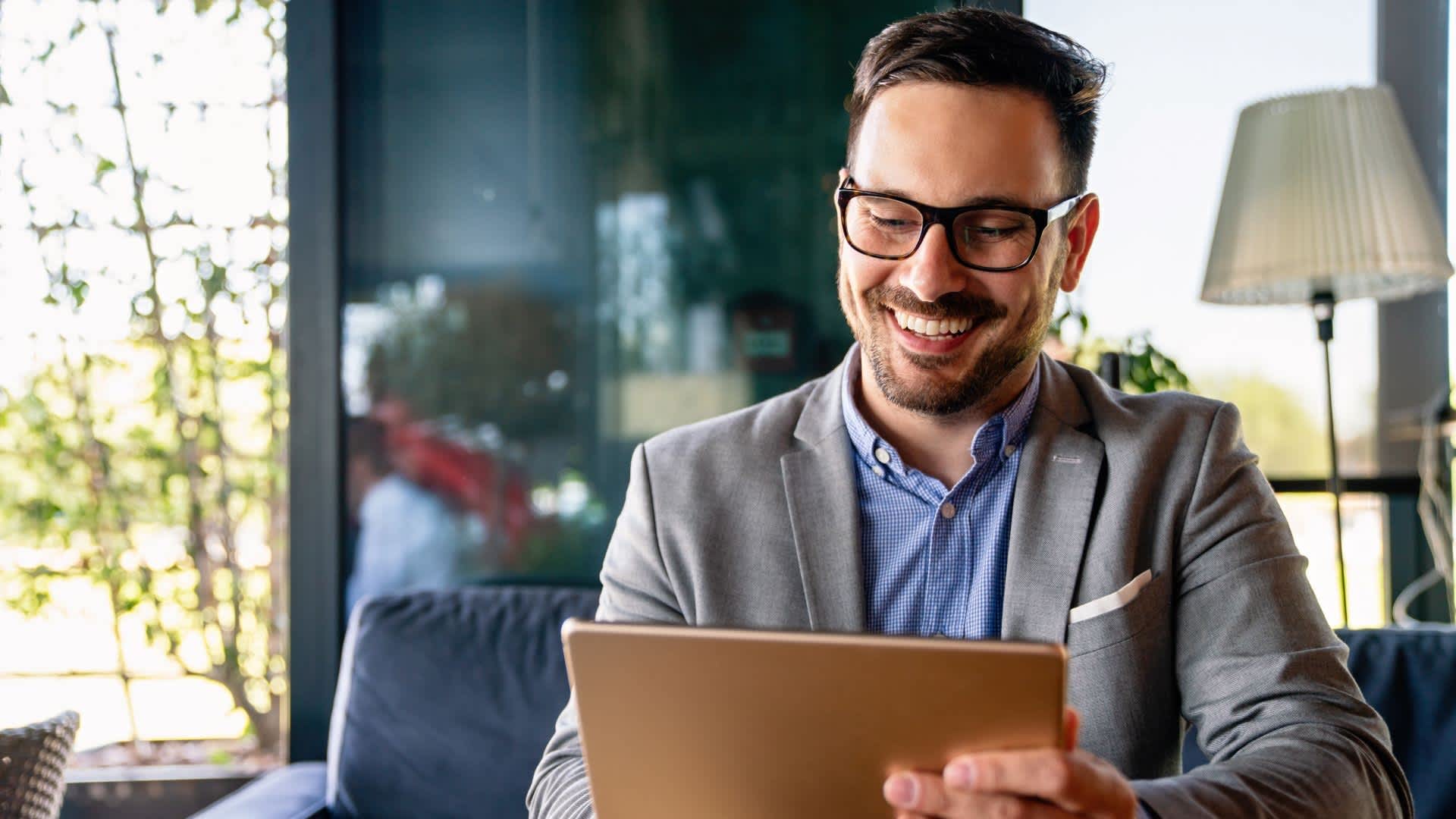 A man wearing glasses is holding a tablet, excited about hospitality management