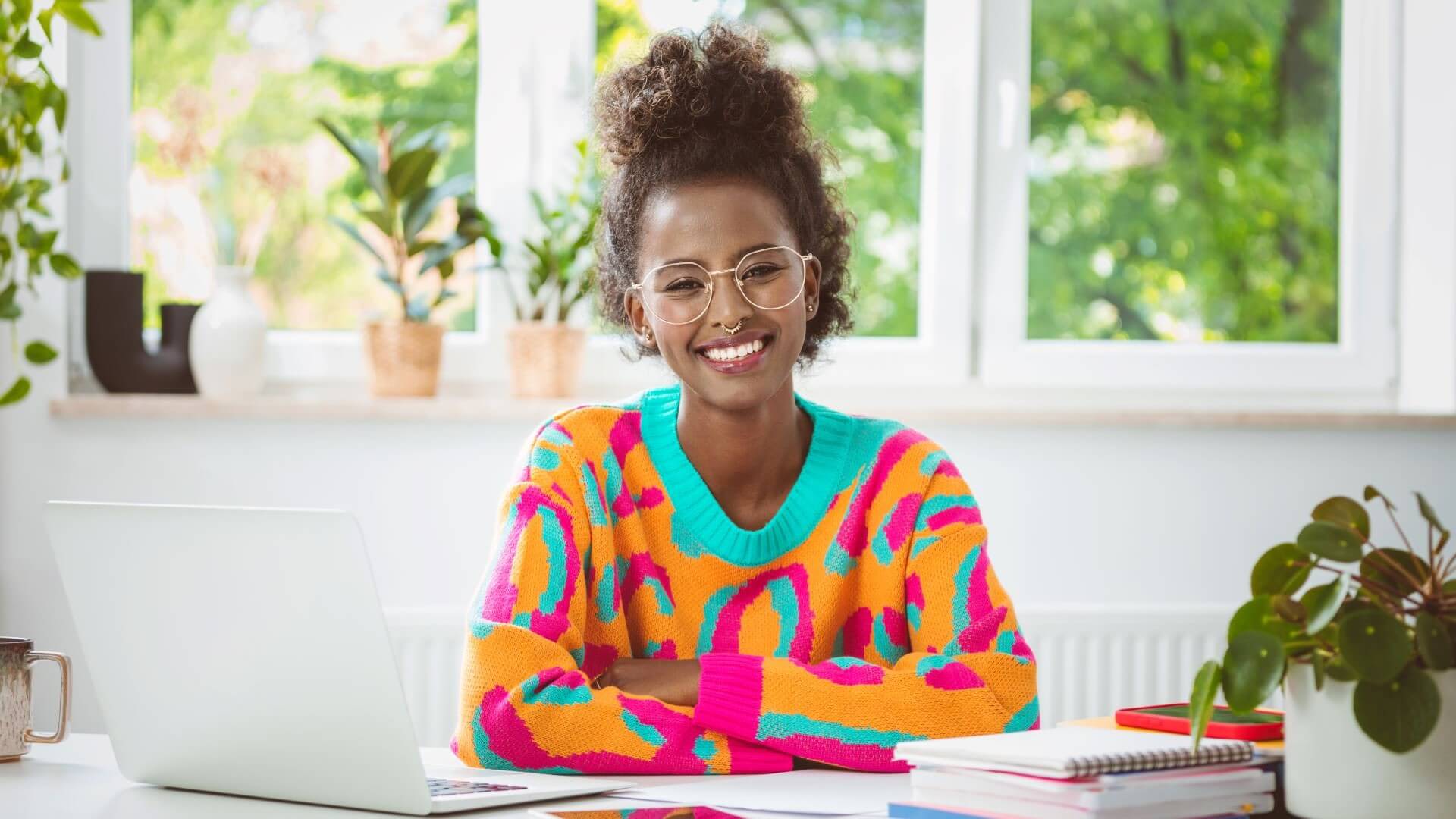 A smiling woman wearing vibrant clothing is sat at a desk studying digital innovation