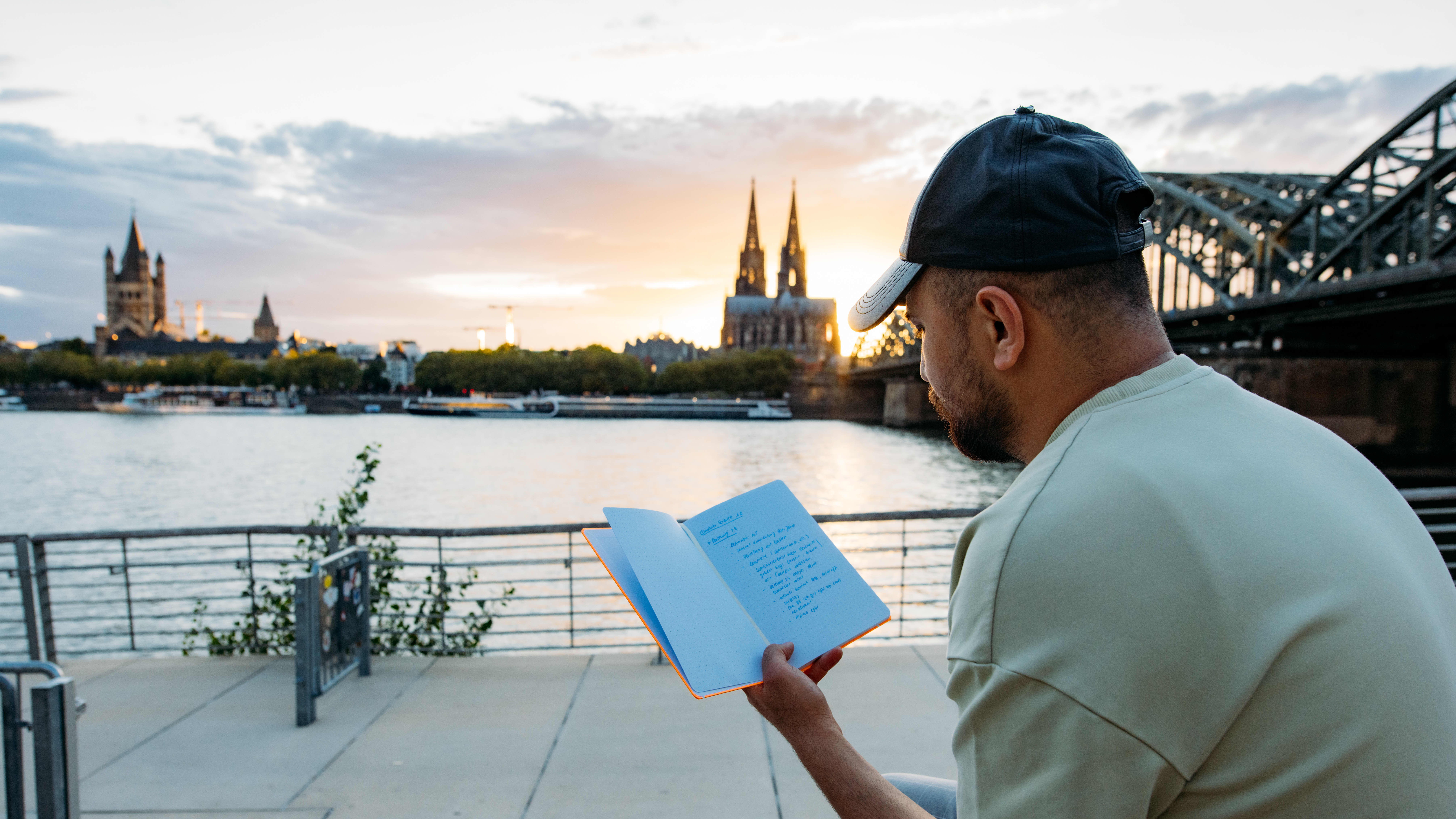 Man sitting and reading a book at sunset in Cologne, with the Cologne Cathedral in the background.