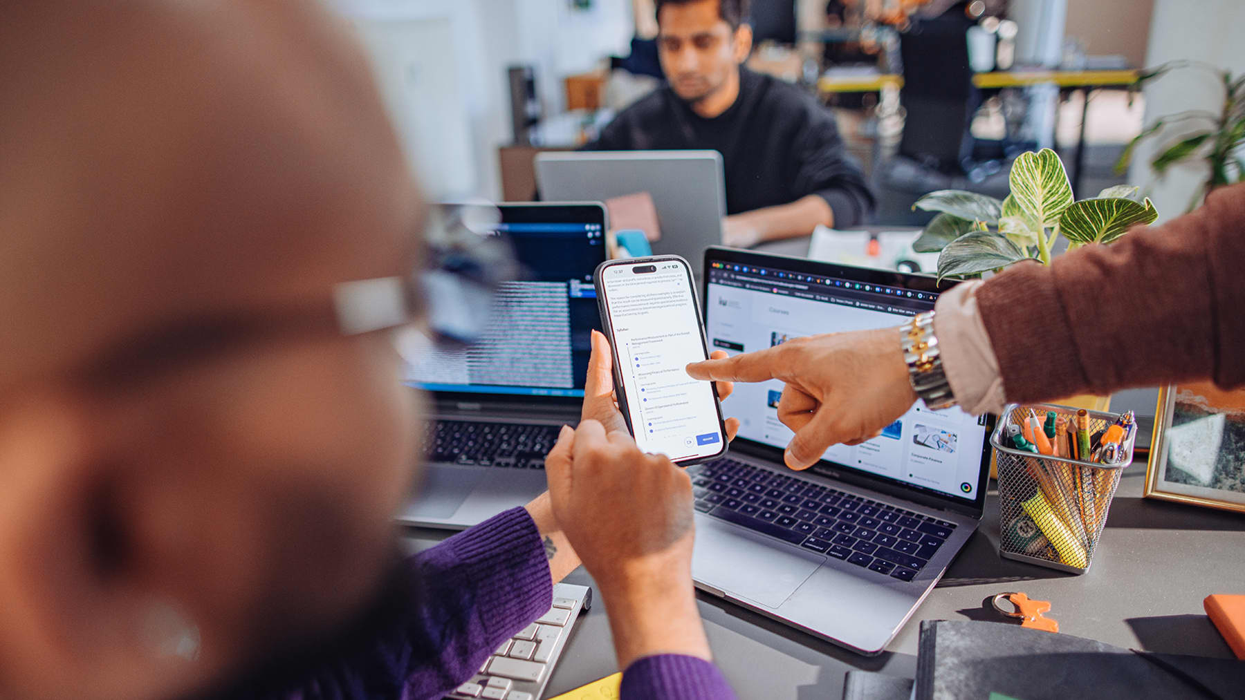 Students observing a mobile phone while working with multiple screens