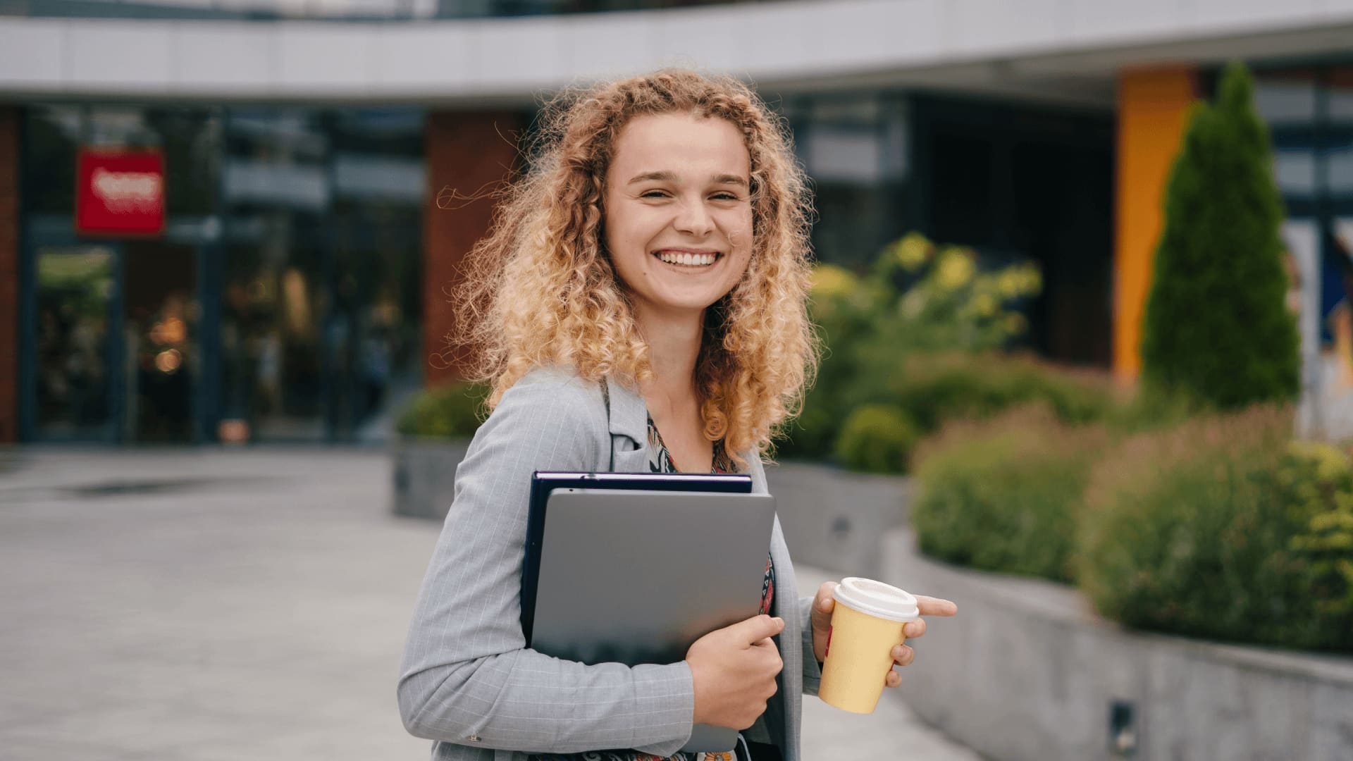 On-campus university student paying on-campus costs carrying a laptop and coffee.