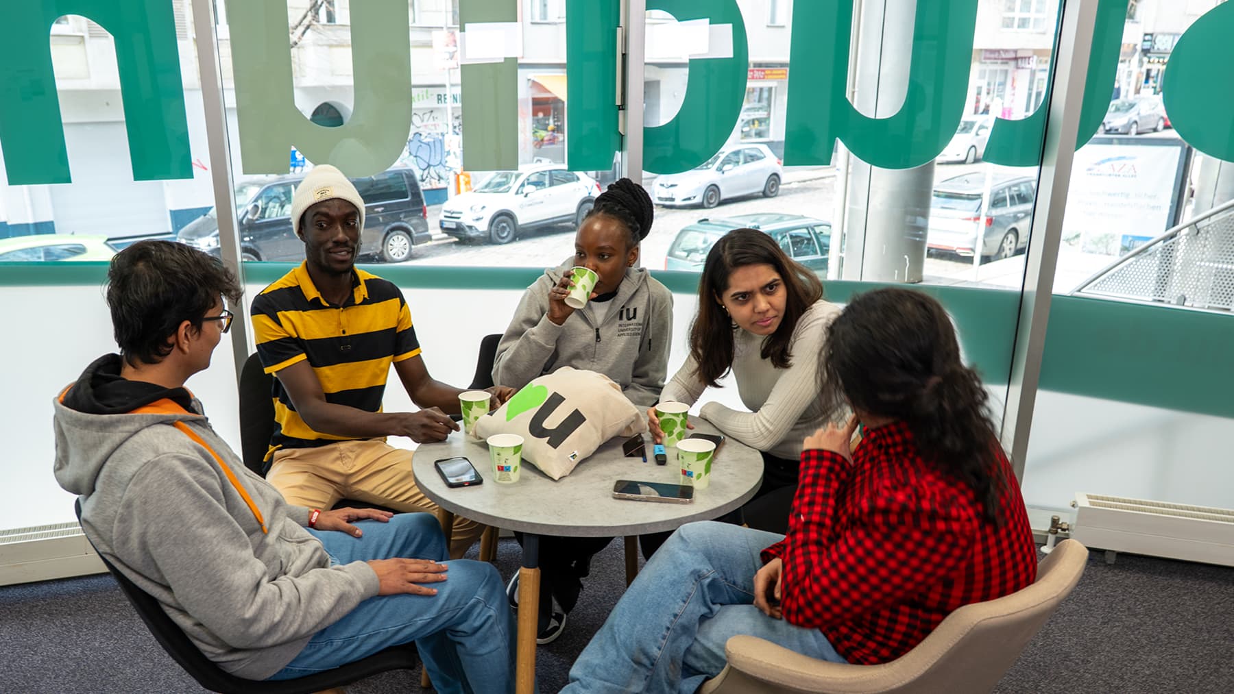 A diverse group of international students socializing and studying together at the IU Berlin campus.