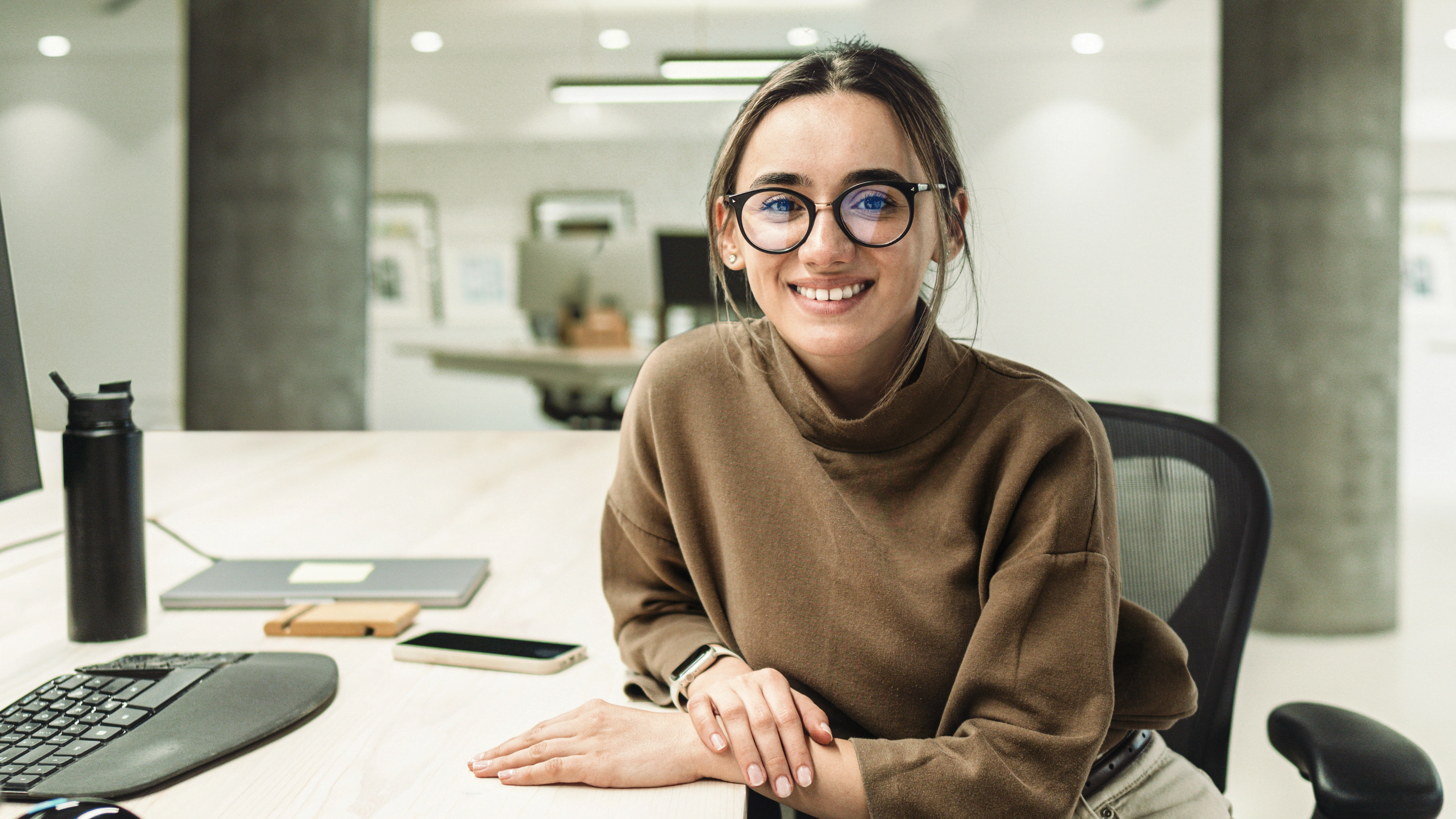 Woman, with glasses, sitting in an office and smiling to the camera