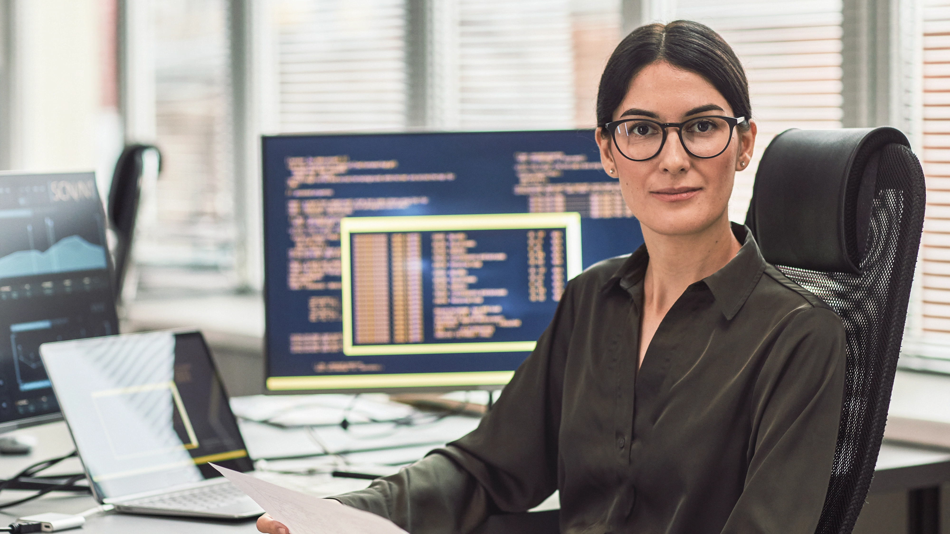 Serious woman holds a paper and looks at the camera while sitting in an office