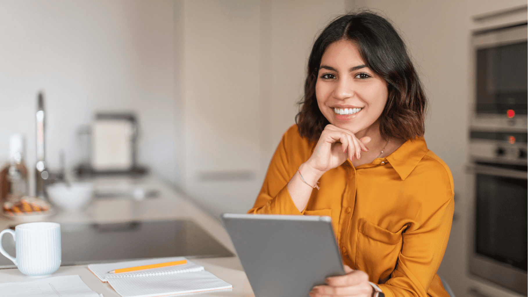 Woman sitting in a kitchen and smiling while holding a tablet