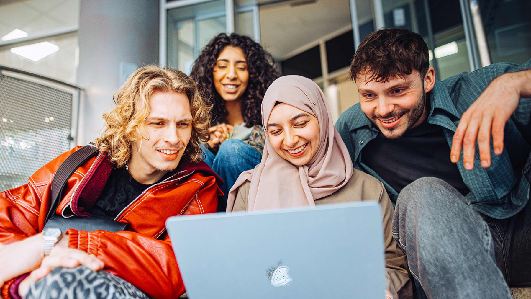 Four smiling students huddle round a laptop
