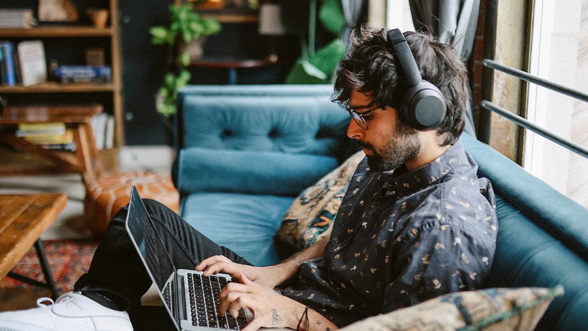 Guy wearing headphones is sitting comfortably in a couch and working on optimising machine learning models