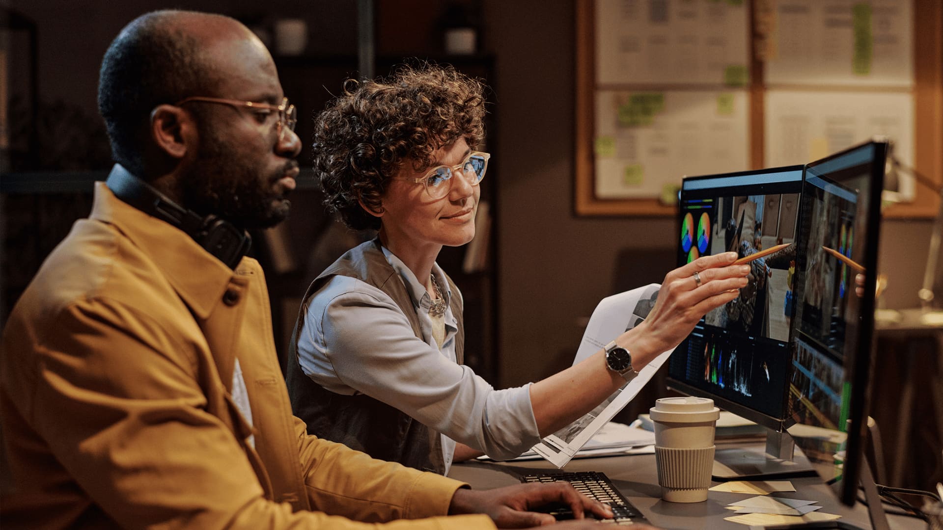 Curly hair woman and bald guy pointing at their desktop and analysing marketing metrics