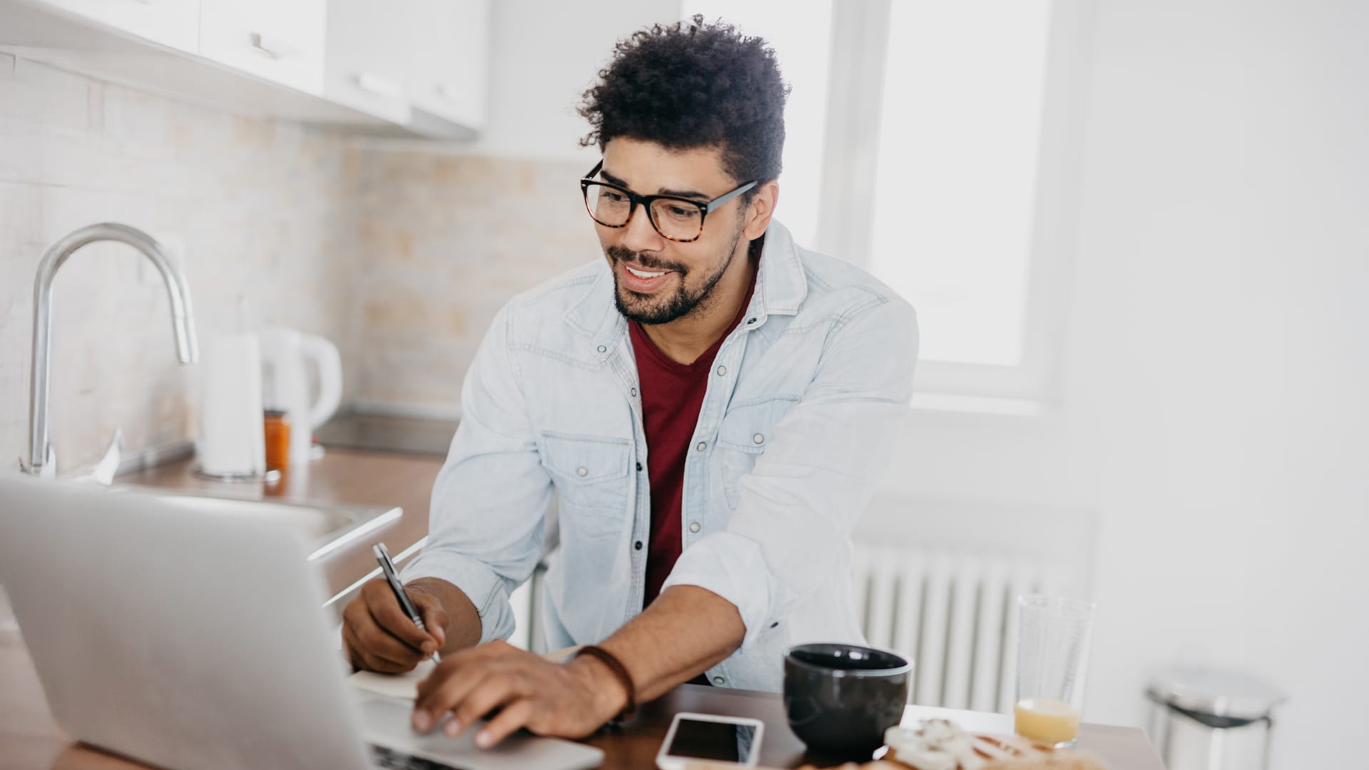 Man with glasses and denim shirt working on business market research from laptop at home.