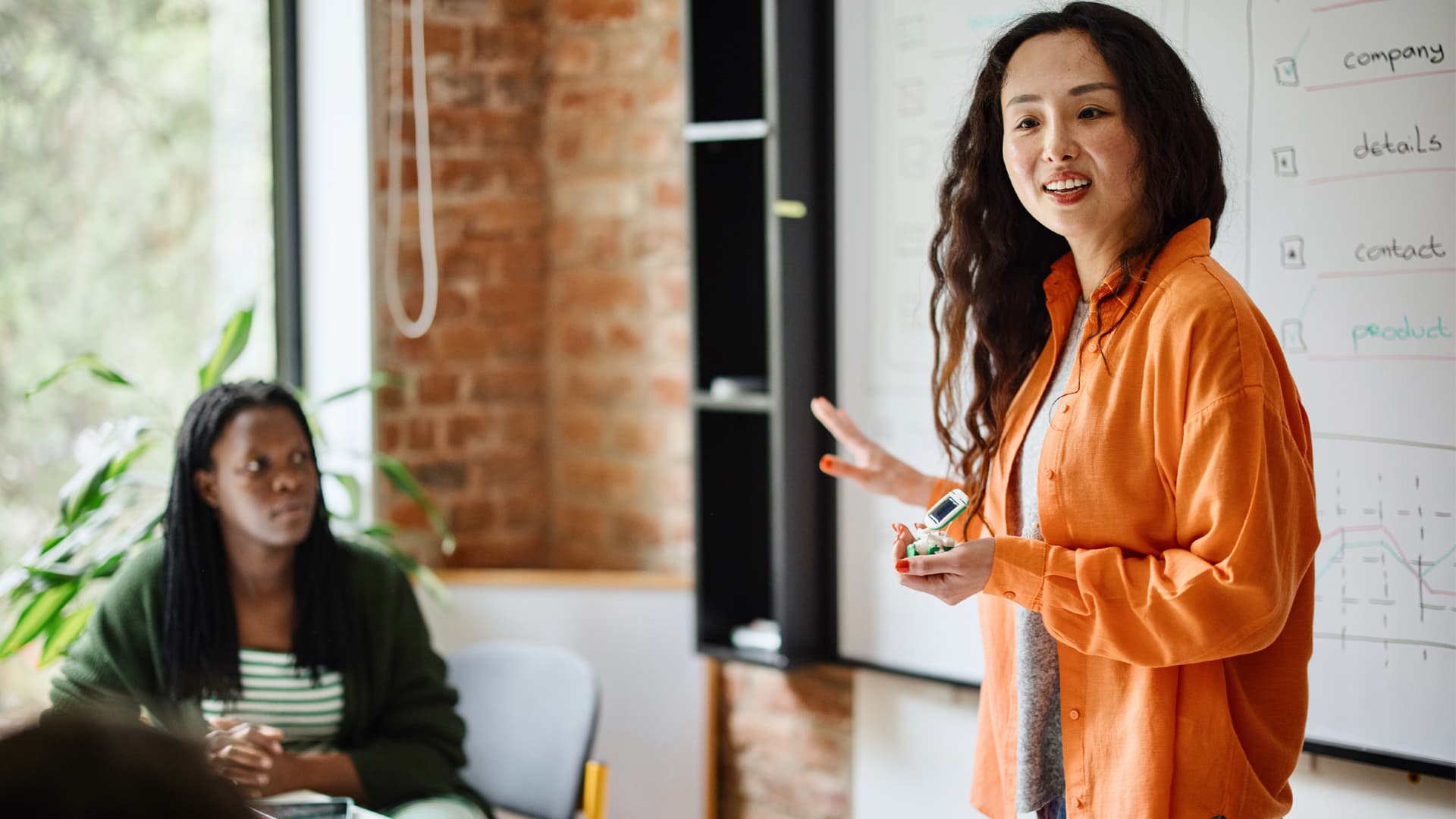 Female business entrepreneur in orange shirt leads MBA students in class on finance.