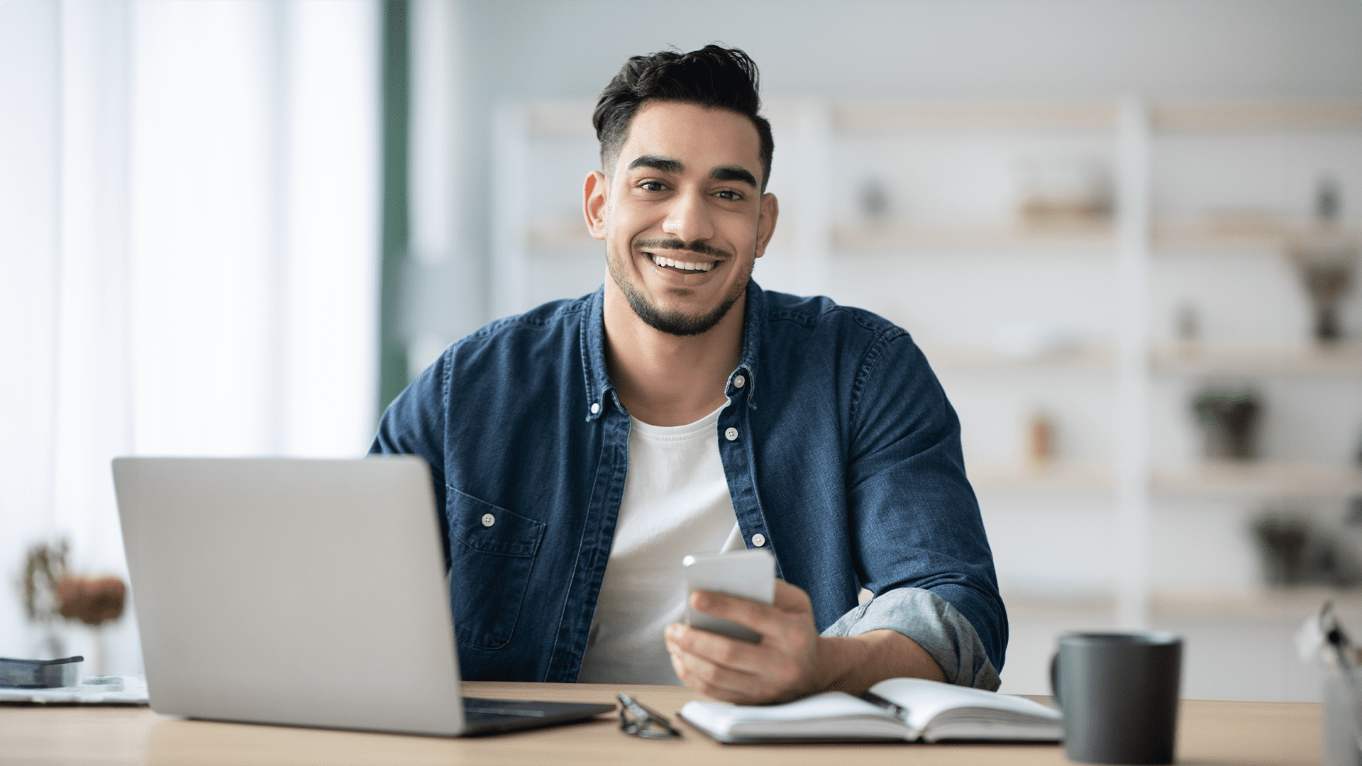 Smiling man sitting at laptop planning to start an accounting business after studying finance.