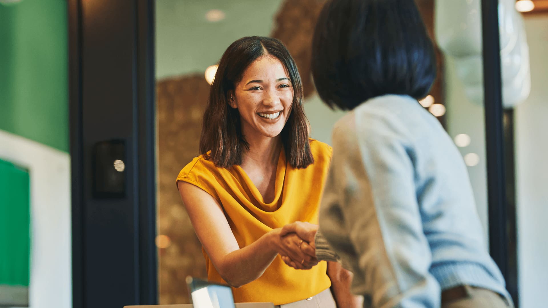 Happy woman in yellow shirt shakes hand with business psychology practitioner.