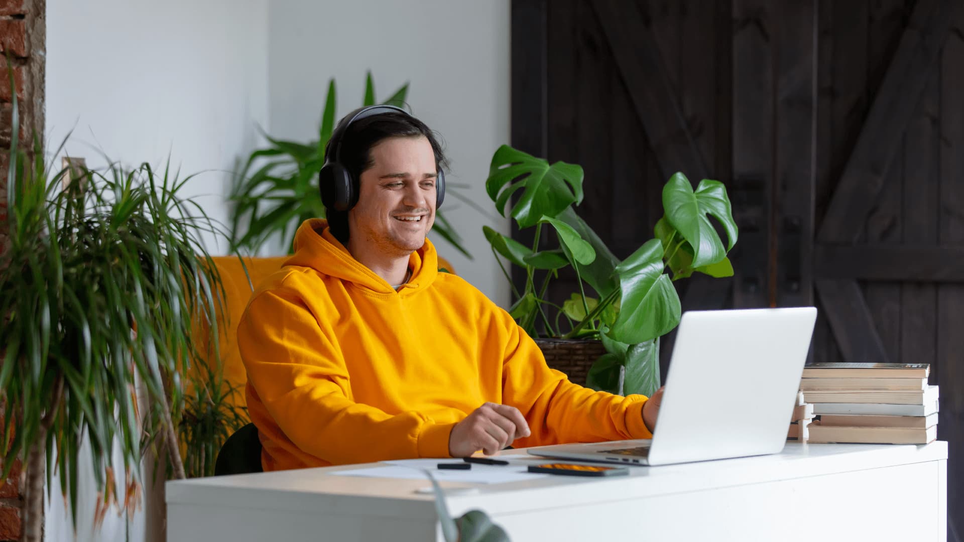 Man wearing an orange hoodie and headphones sitting at a desk is working with algorithms and data sets