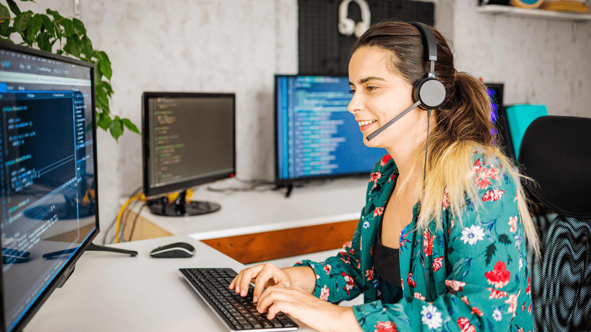 Happy woman with headset sat at multiple screens reviewing network security