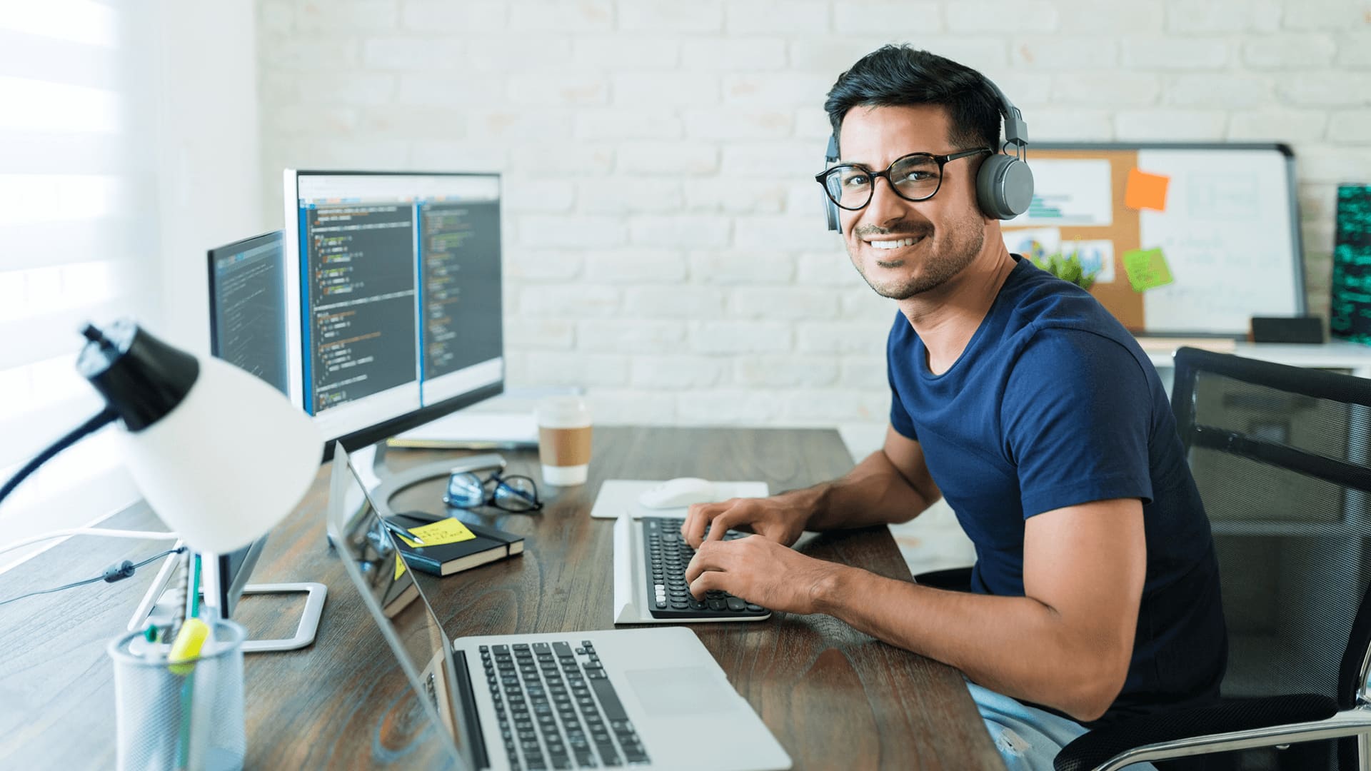 Guy wearing glasses and a blue t-shirt typing on his laptop and designing software applications