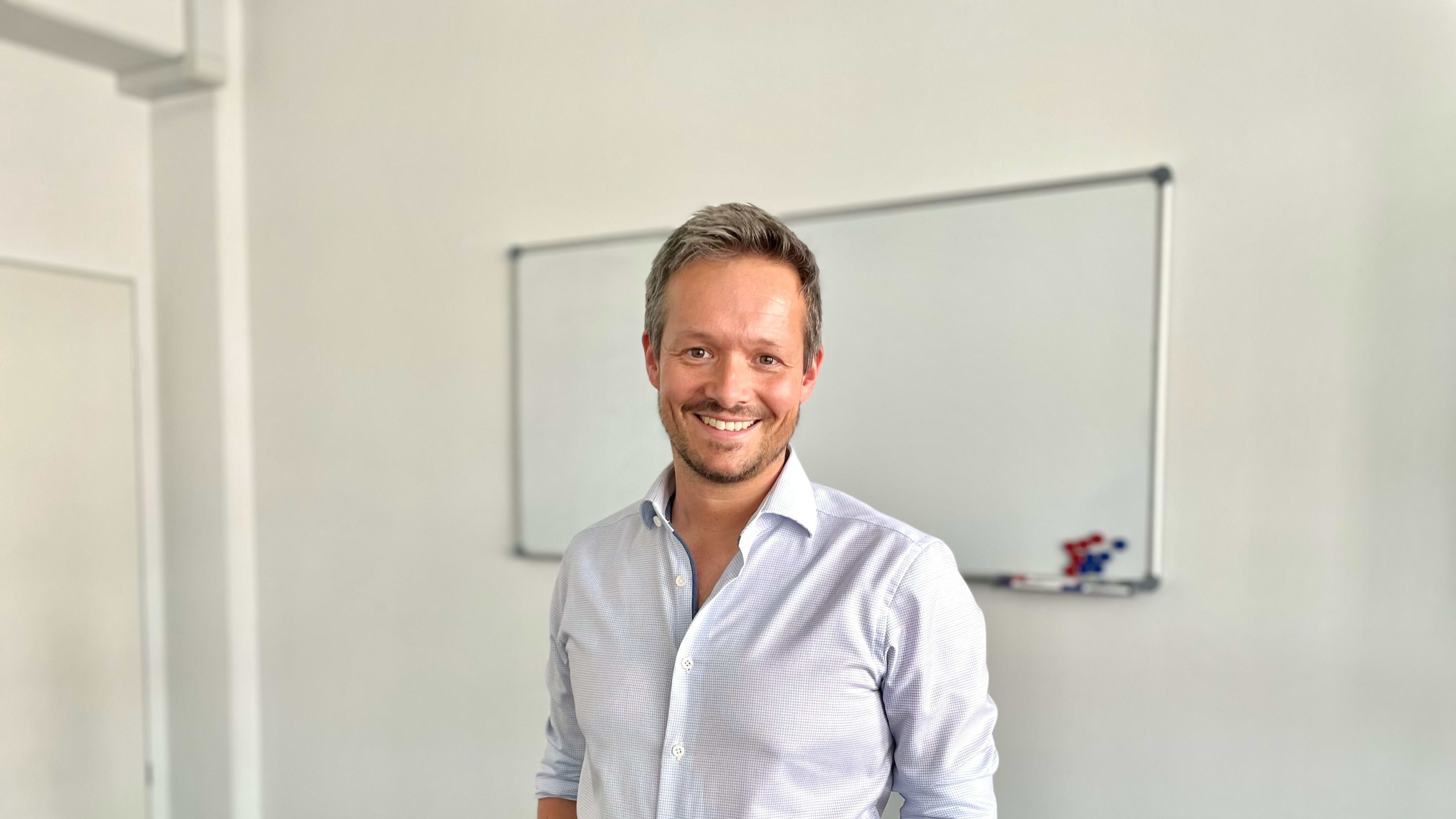 Lächelnder Mann im Business-Hemd steht in hellem Büro vor Whiteboard.