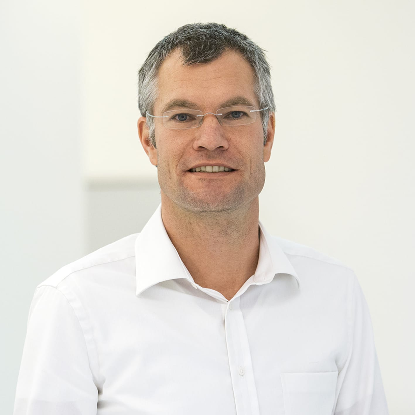 Lächelnder Mann mit Brille im weißen Hemd vor hellem Hintergrund
