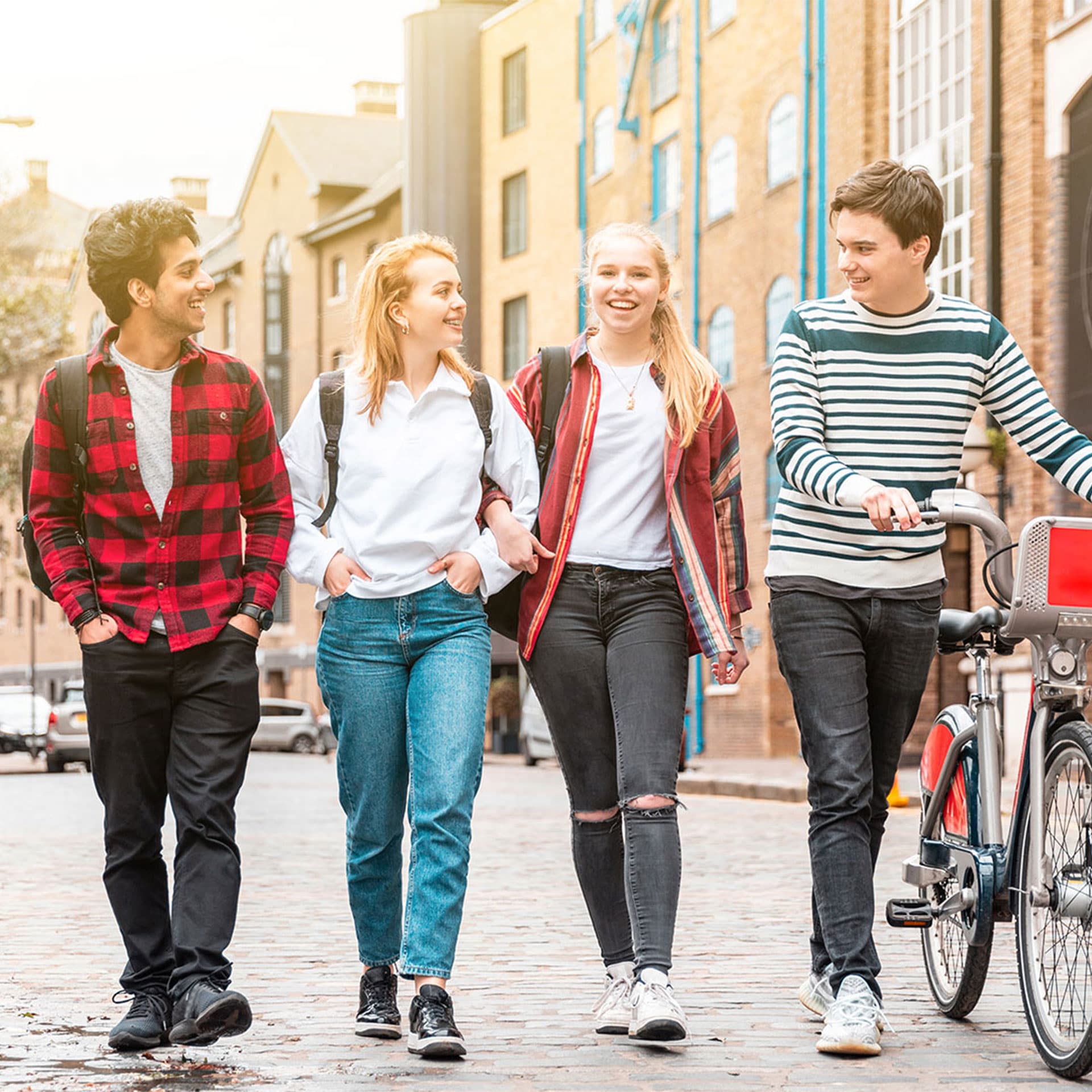 A young group of people walking, smiling and one of them is holding a bicycle.