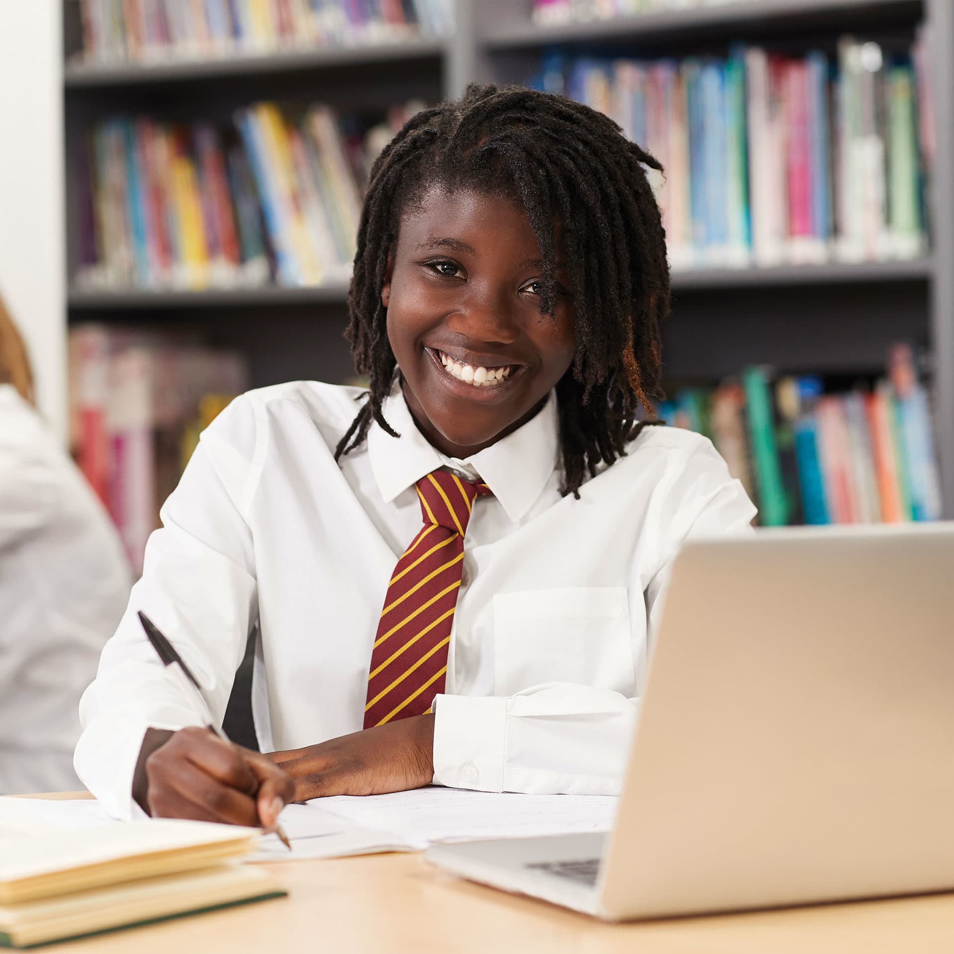 A young girl in school writing in her notebook and smiling.