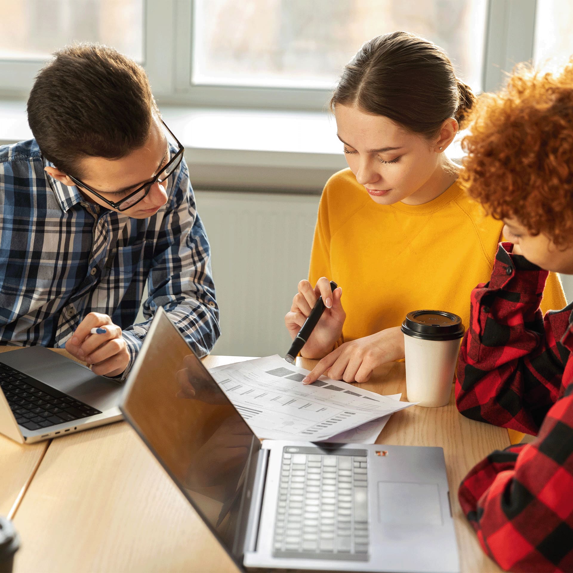 Young group of people with laptops looking over papers.