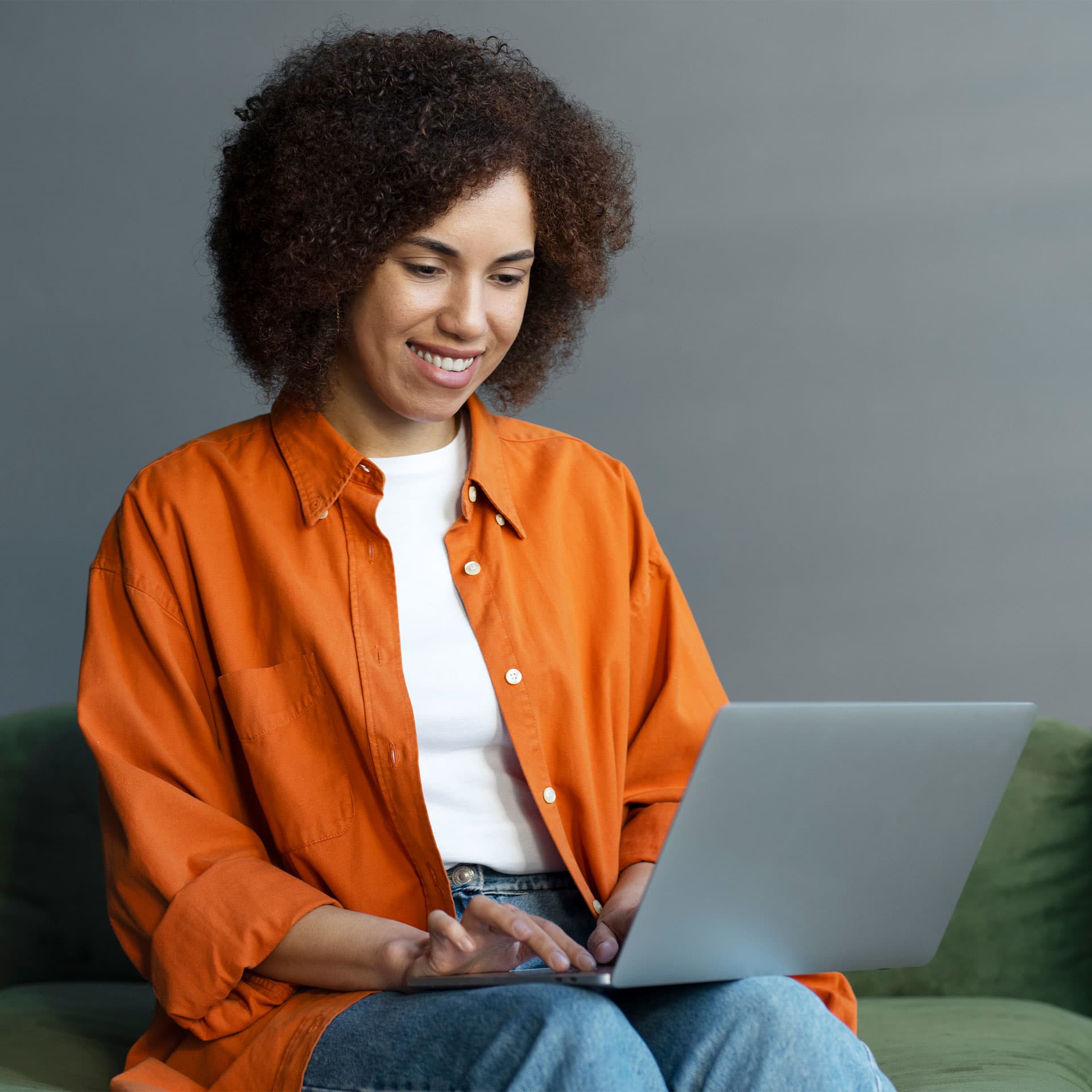 A woman sitting on the sofa, smiling and looking at her laptop.