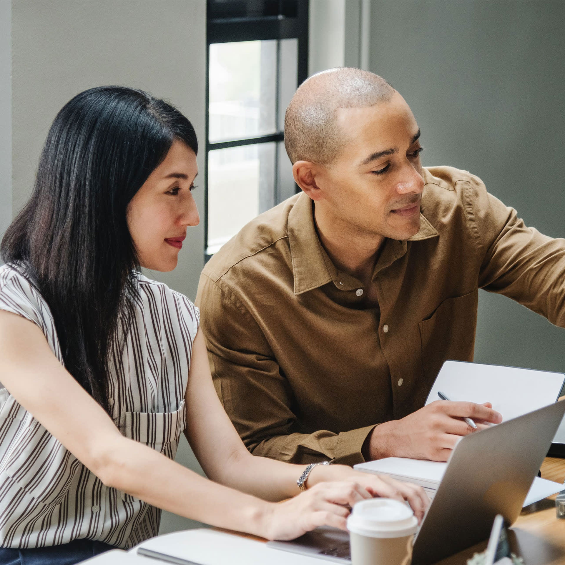 Two professionals, including a credit expert, collaborating on a project while looking at a laptop screen in a modern office setting.