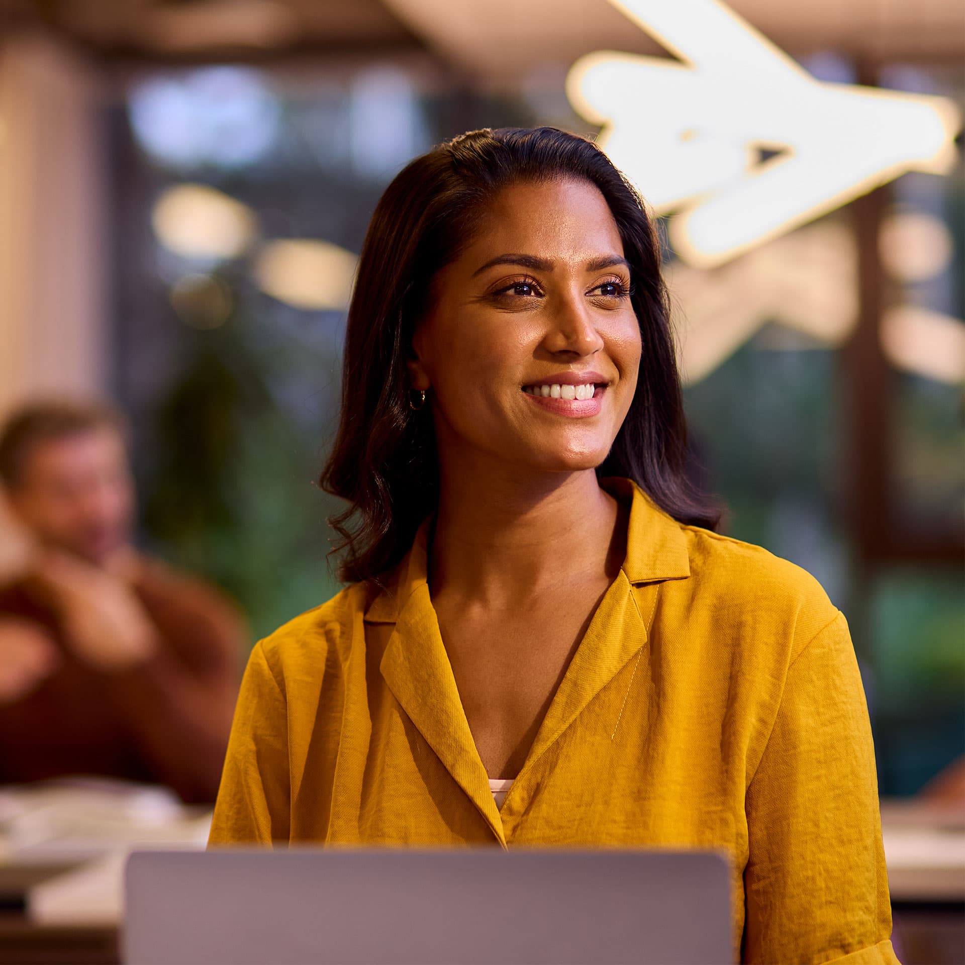 A young woman sitting at a desk with a laptop and looking ahead.