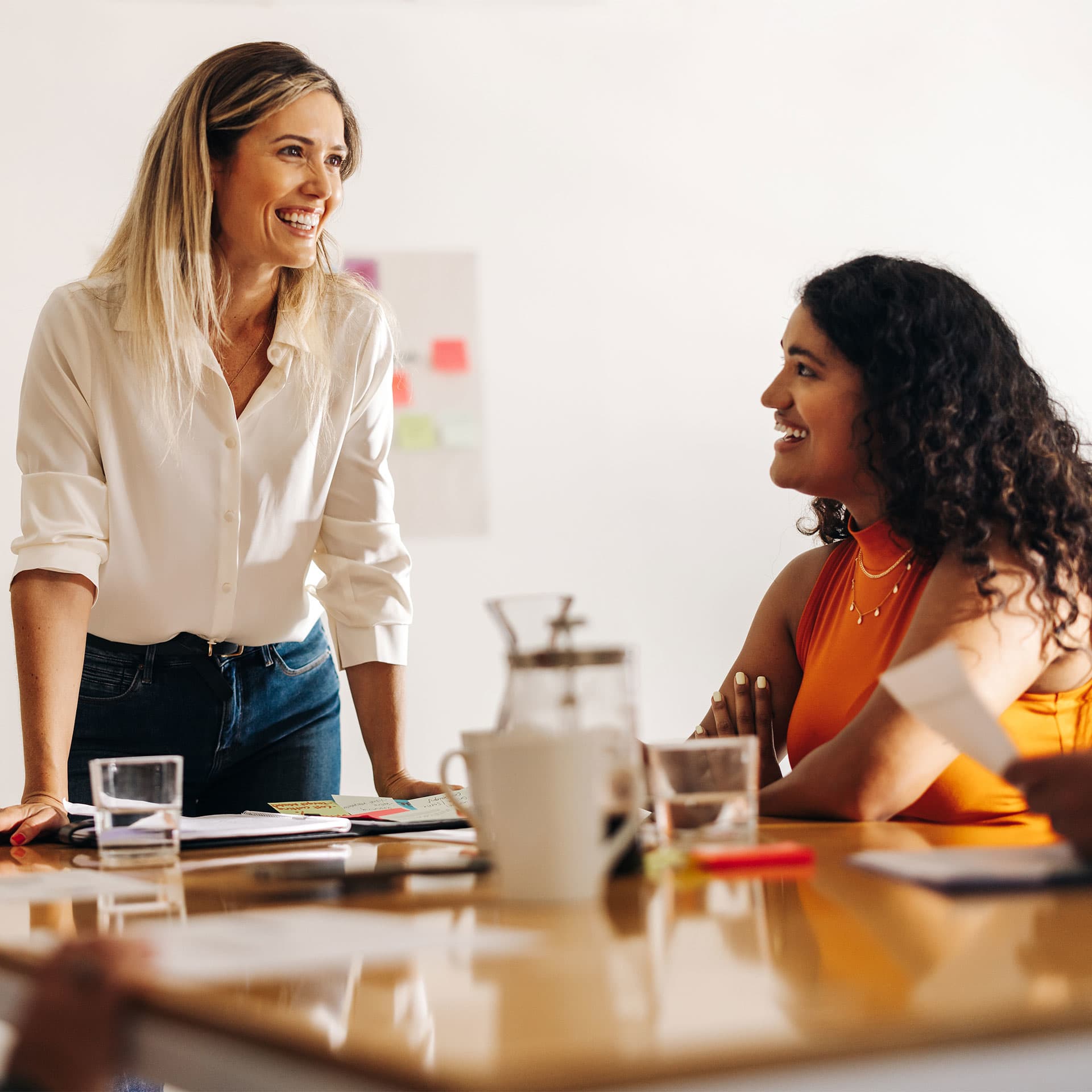 Two women sharing a cheerful moment in a bright office space, while they are working to get their CPSP qualification.