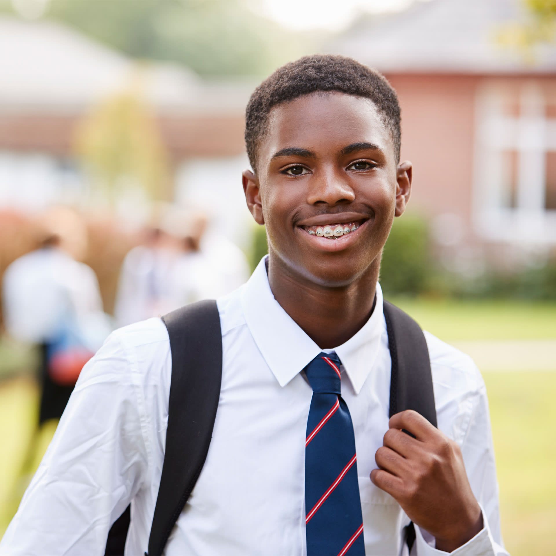 A young boy smiling, wearing a school uniform and a backpack.