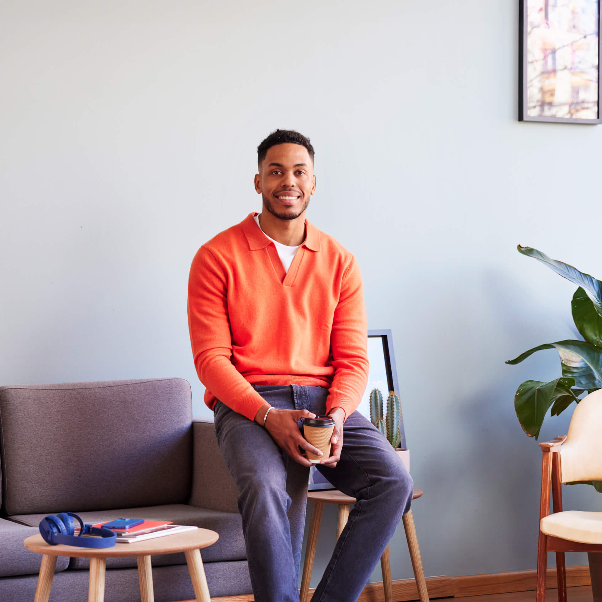 Man wearing an orange sweater and holding coffee seems happy to talk about his cyber security professional life