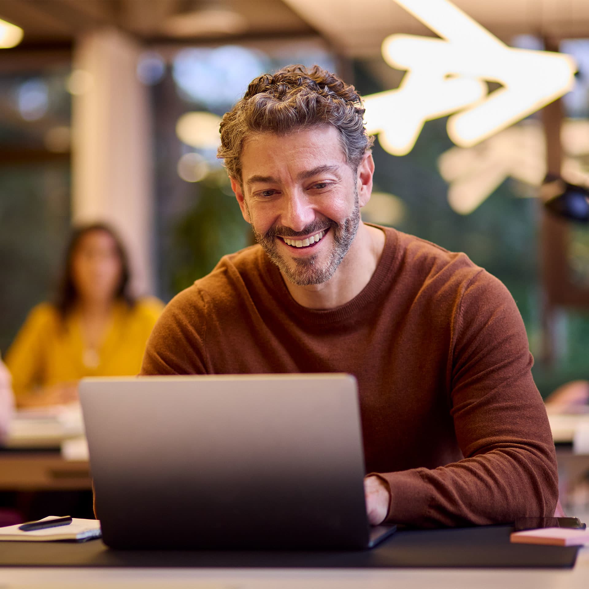 A man sitting at a desk with his laptop and smiling.