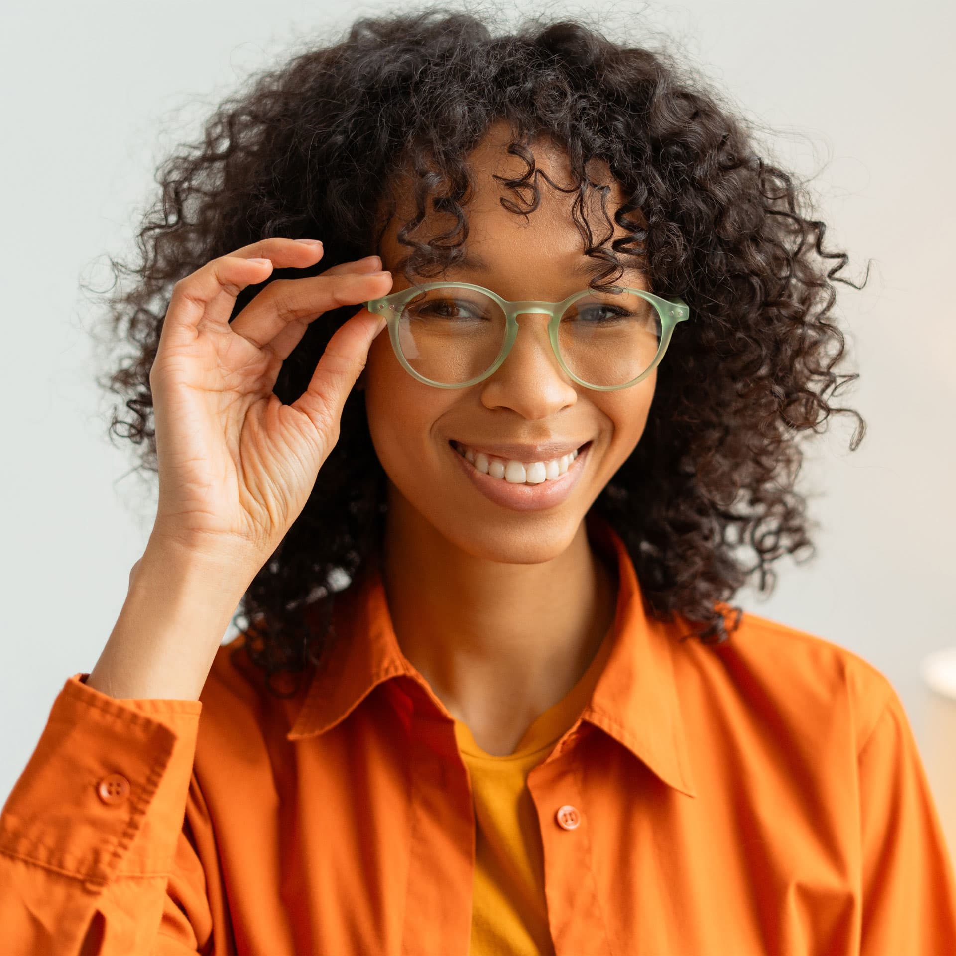 A woman holding her glasses and smiling.
