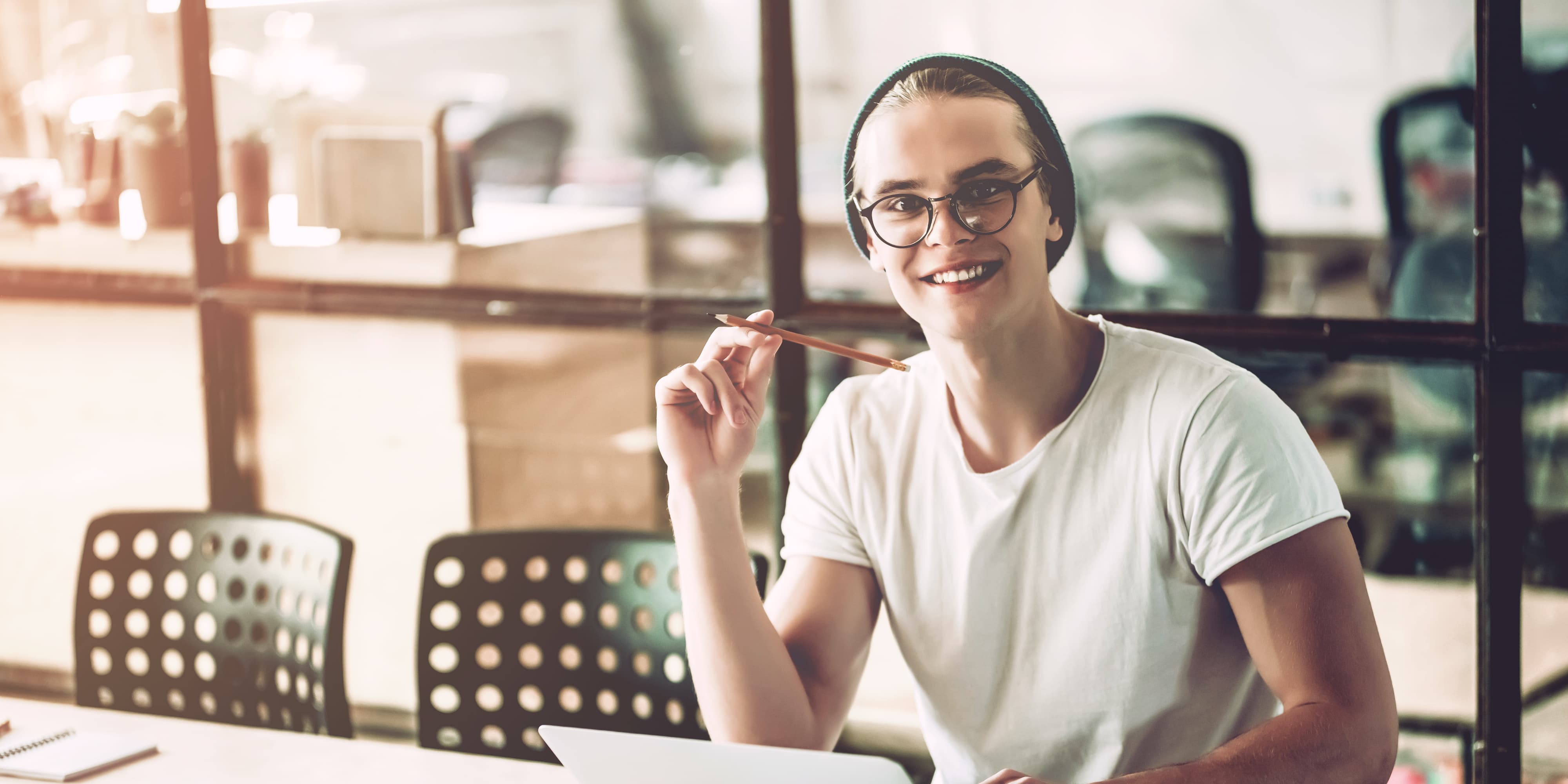 Titelbild für Infoseite “duales Studium Marketingmanagement": Lächelnder Student am mit Laptop am Schreibtisch