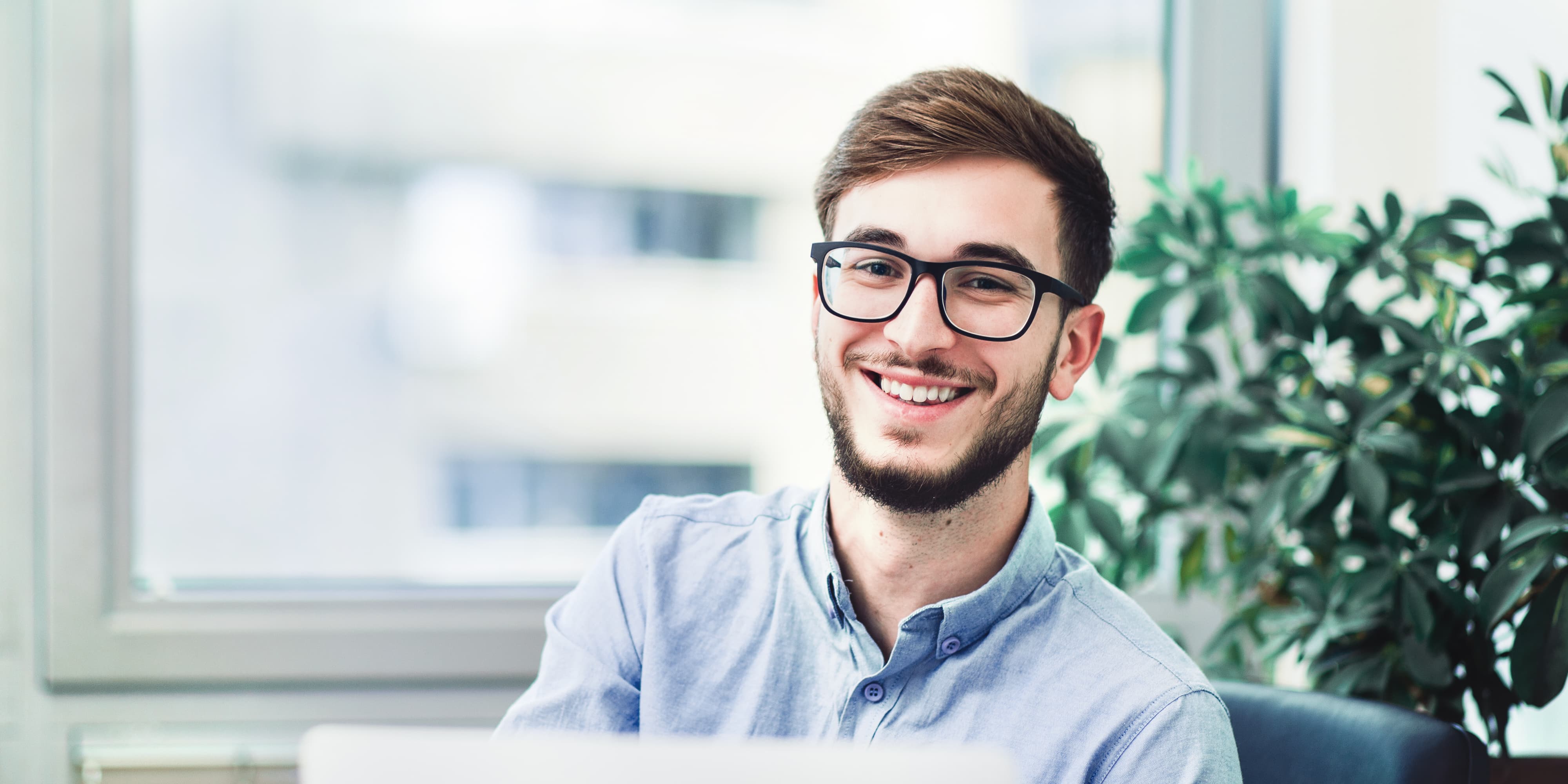 Titelbild für Infoseite “duales Studium BWL Accounting & Controlling": Dualer Student mit Brille sitzt in Büro vor seinem Laptop