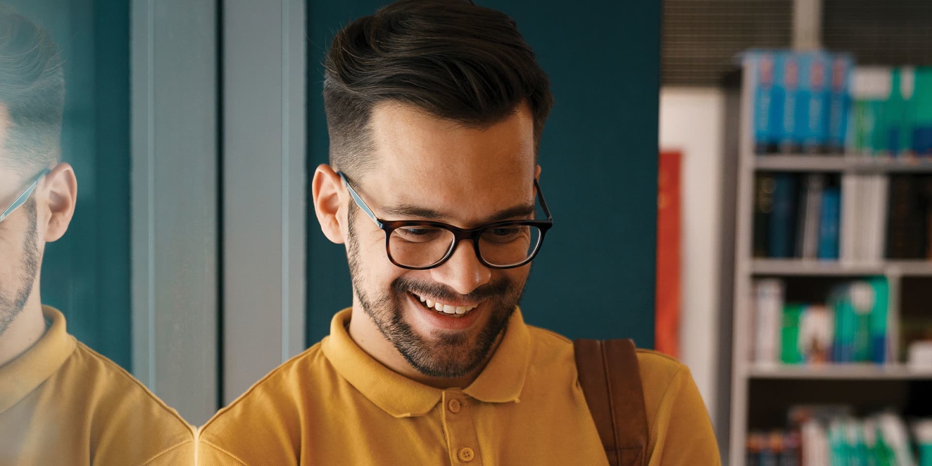 Young man wearing glasses standing, holding an ipad smiling.