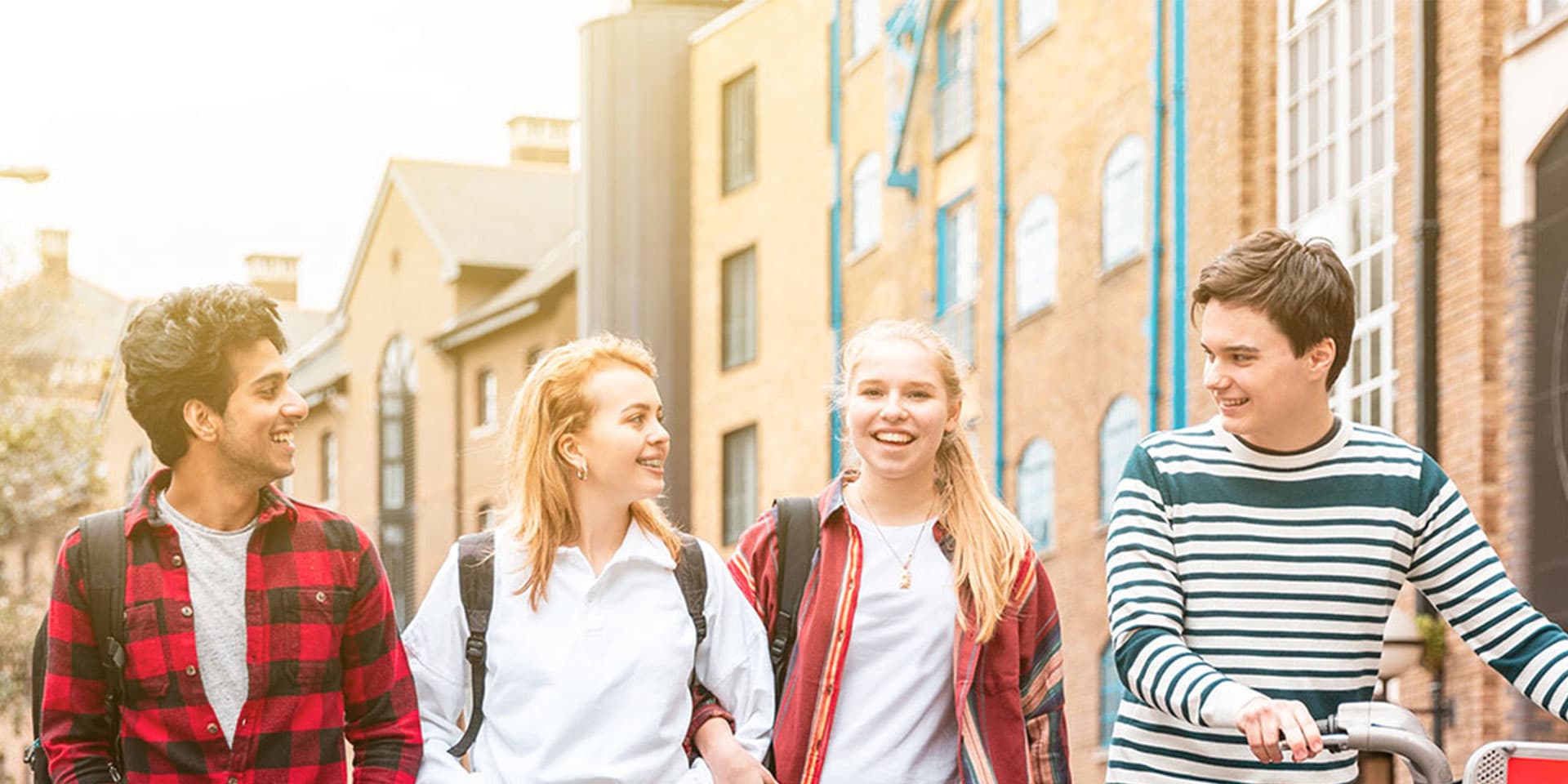 A young group of people walking, smiling and one of them is holding a bicycle.